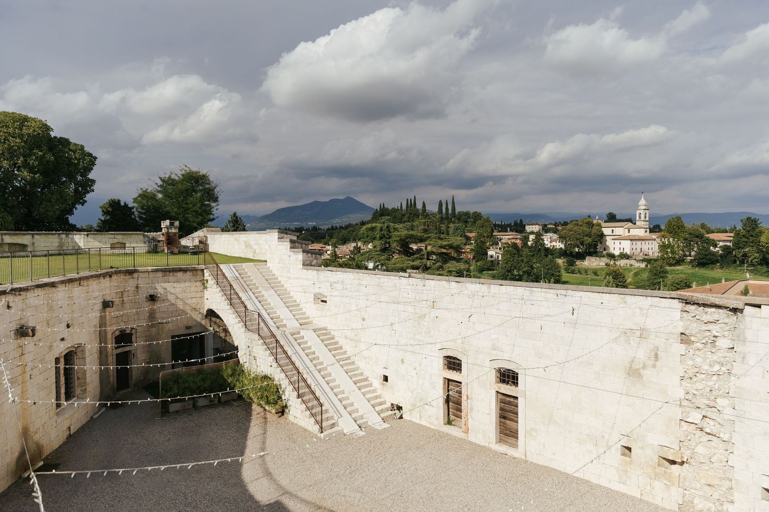 Stone building exterior with white walls and stairs under dramatic cloudy sky.