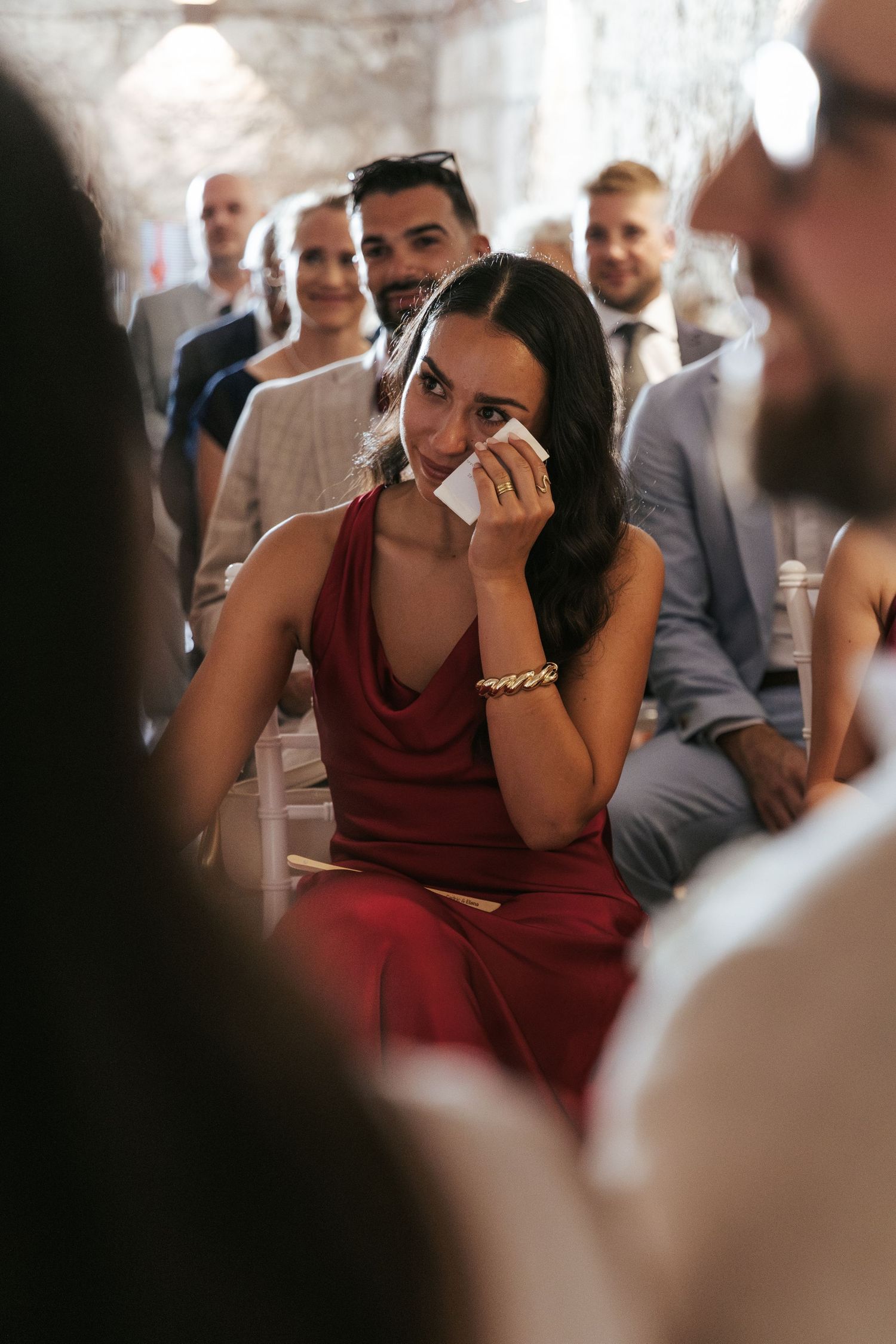 Wedding guest in burgundy dress shows emotional reaction during ceremony.