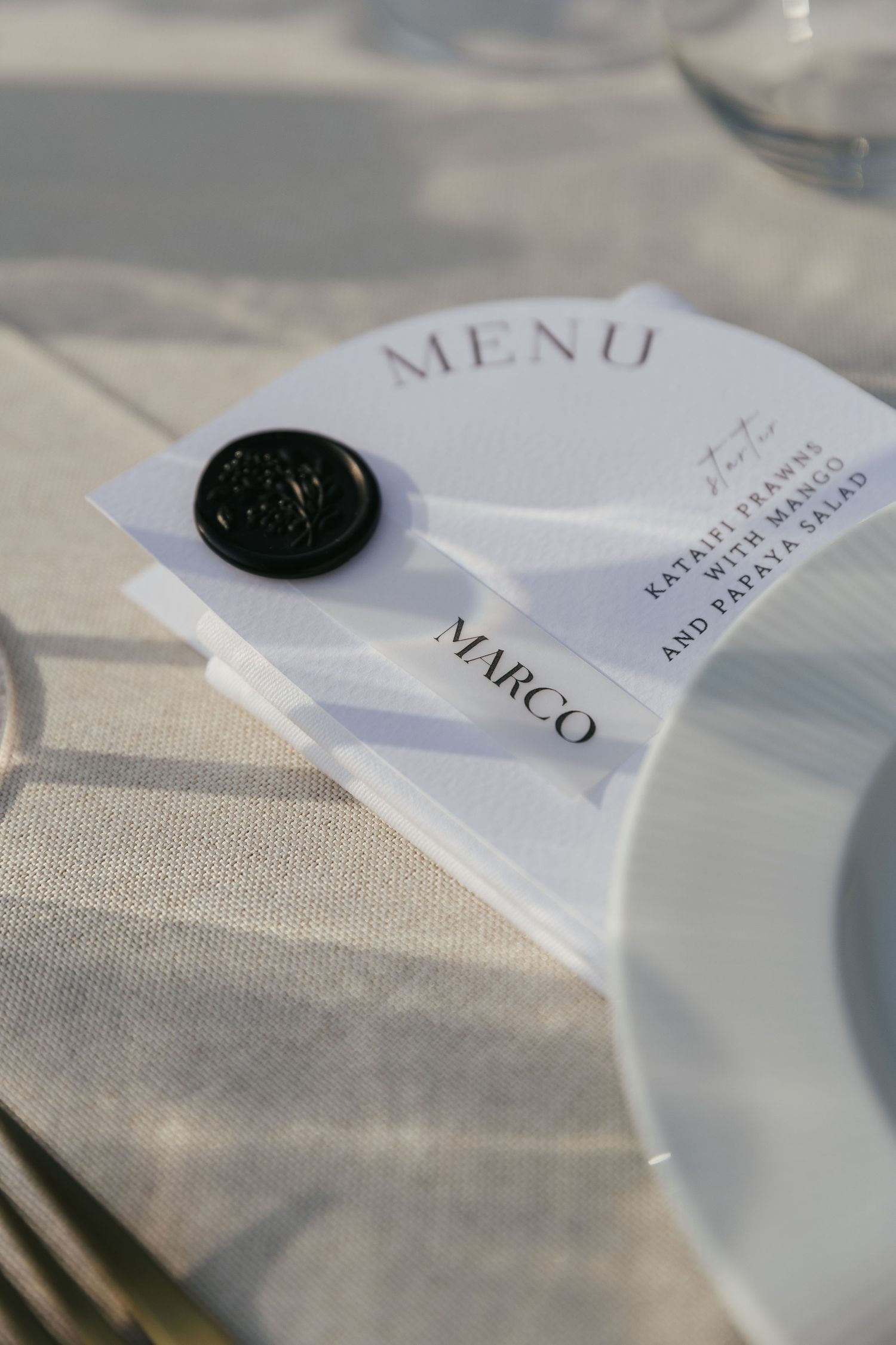 Elegant menu cards with minimalist typography and wax seals lay on a textured linen tablecloth in soft lighting.