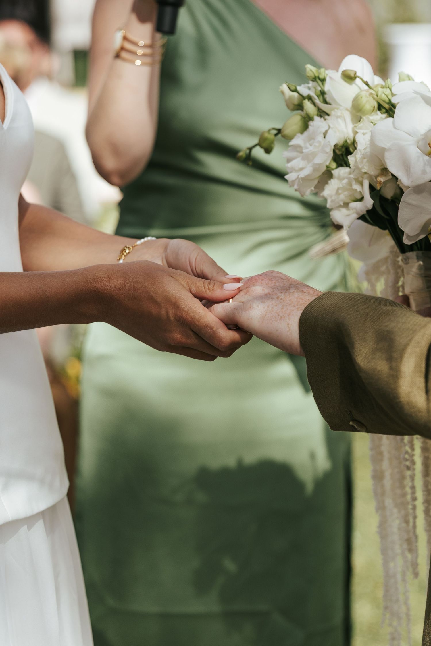 Bride and groom holding hands during wedding ceremony with bridesmaid in green dress holding white bouquet.