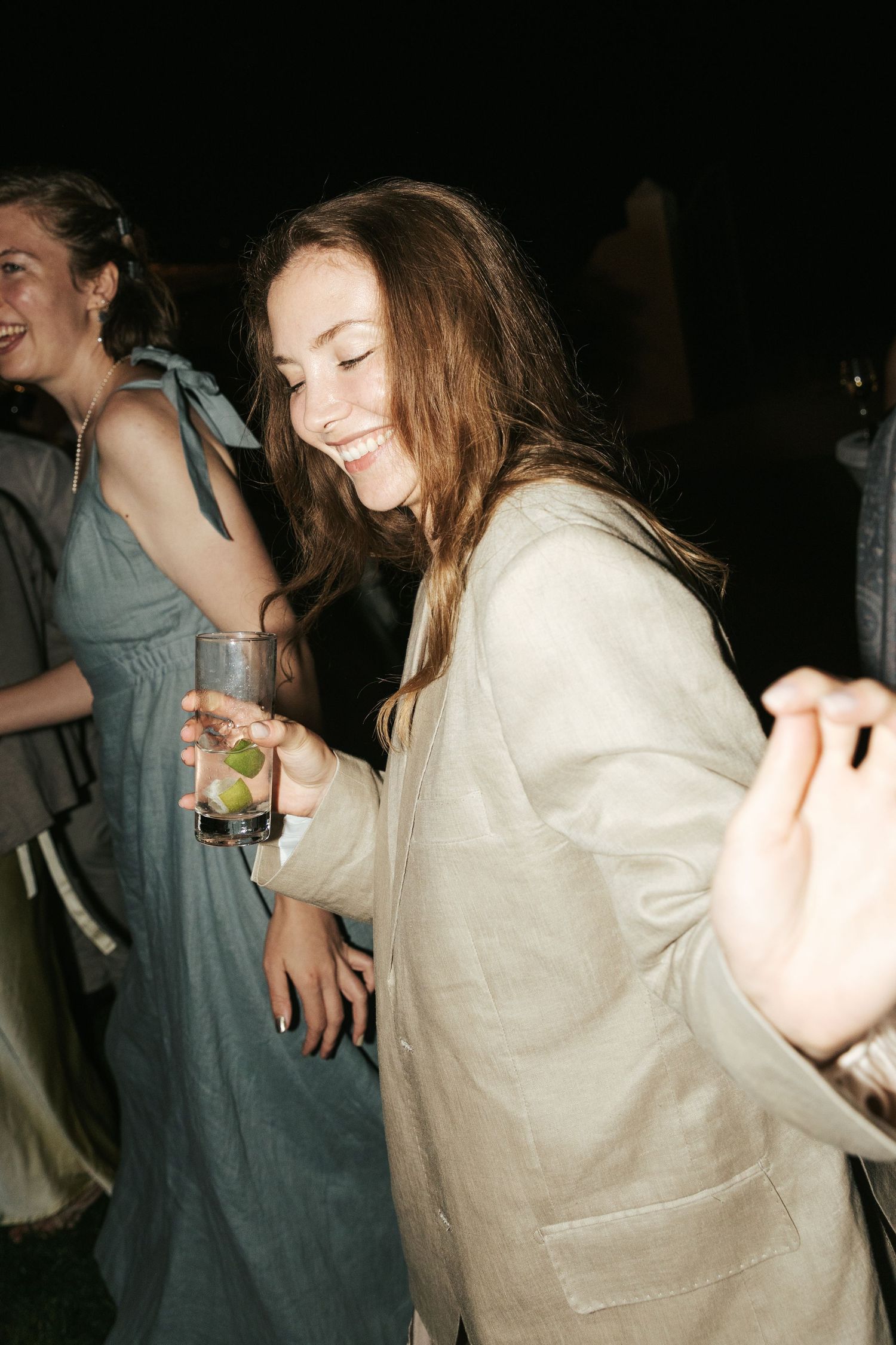 Young woman in linen jacket laughs while dancing at an outdoor evening wedding reception.