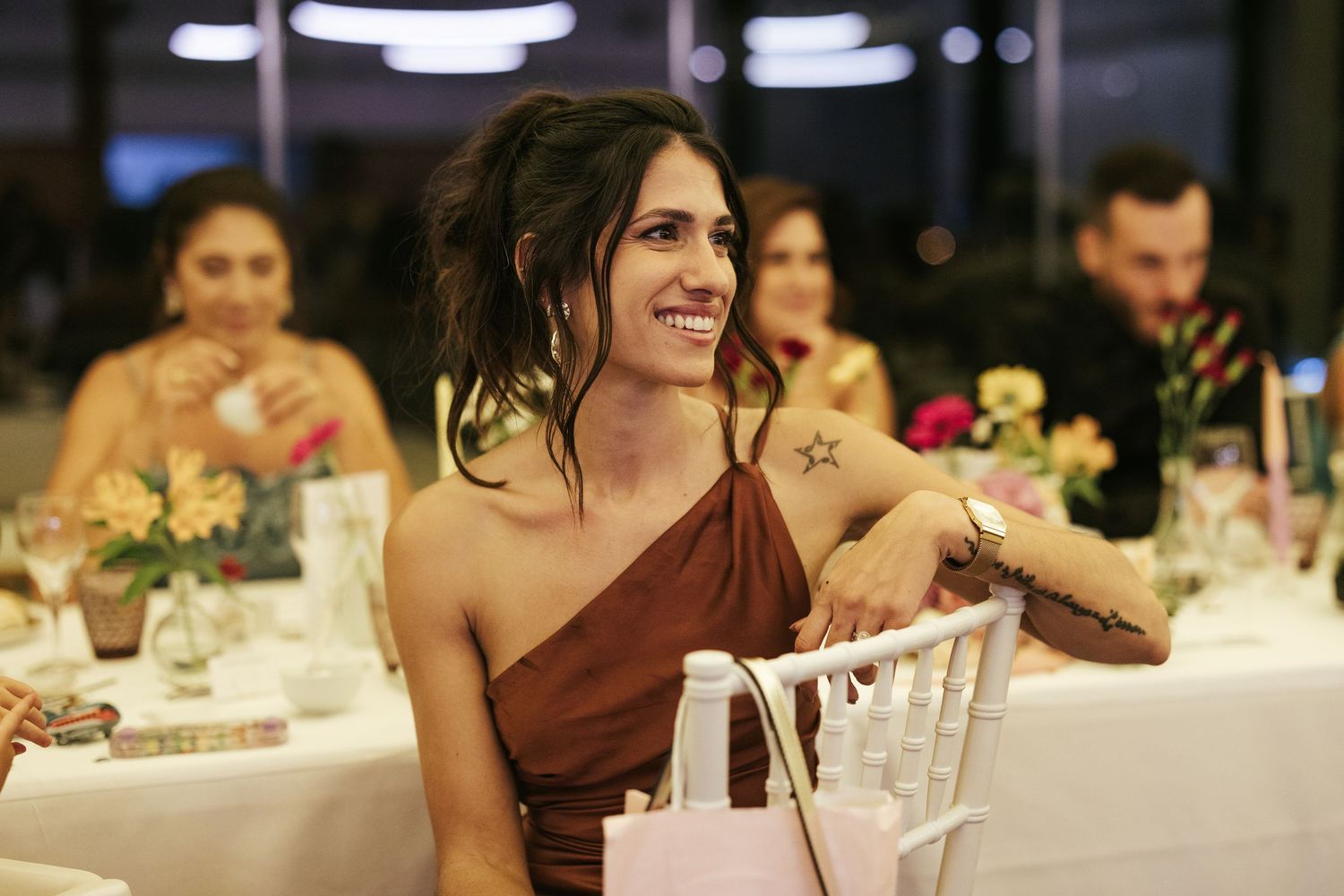 A guest in a burgundy one-shoulder dress smiles during an evening wedding reception celebration.