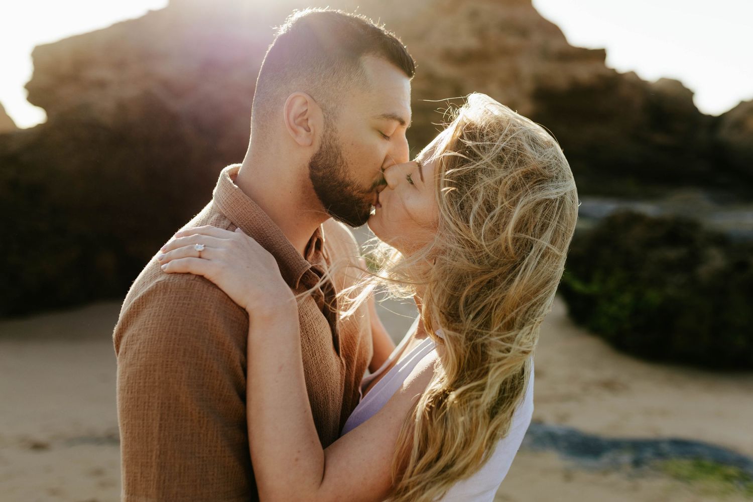 Romantic couple embraces on sandy beach during golden hour sunset.