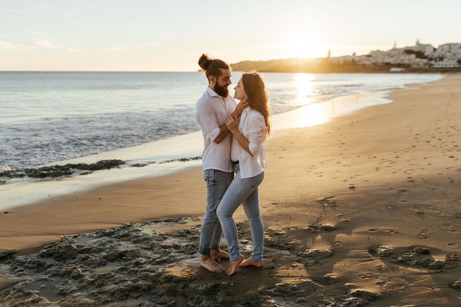 A couple dances together on a sandy beach at sunset with ocean waves in the background. Praia da Luz, Lagos, Algarve, Portugal.
