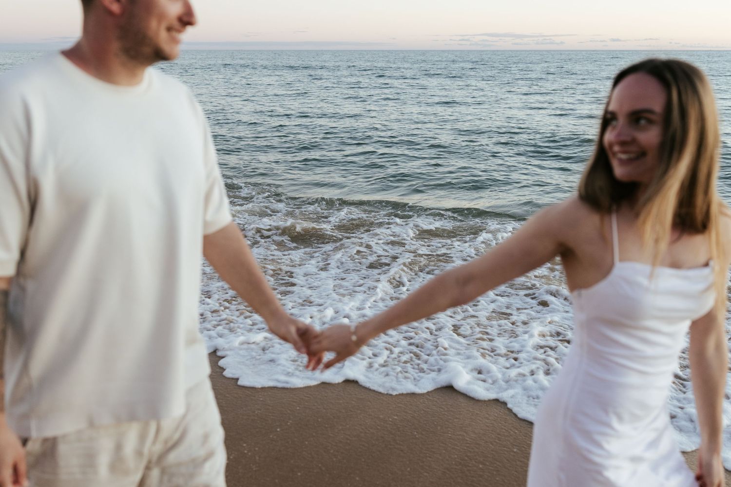 A couple holding hands on the beach at sunset while walking along the ocean shore.