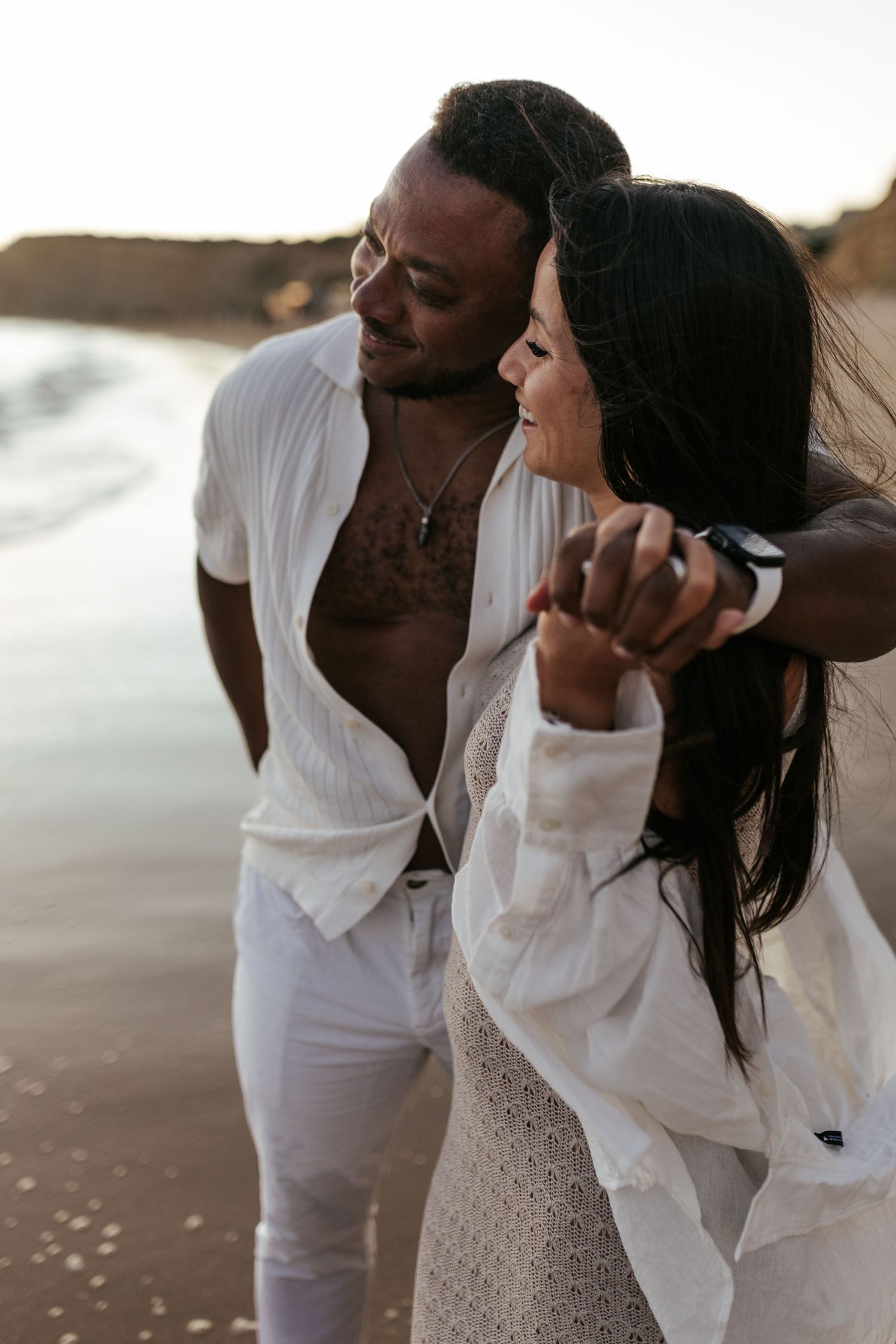 Romantic couple in white outfits sharing an intimate moment on a beach at sunset. Praia do Porto de Mós, Lagos, Algarve, Portugal.