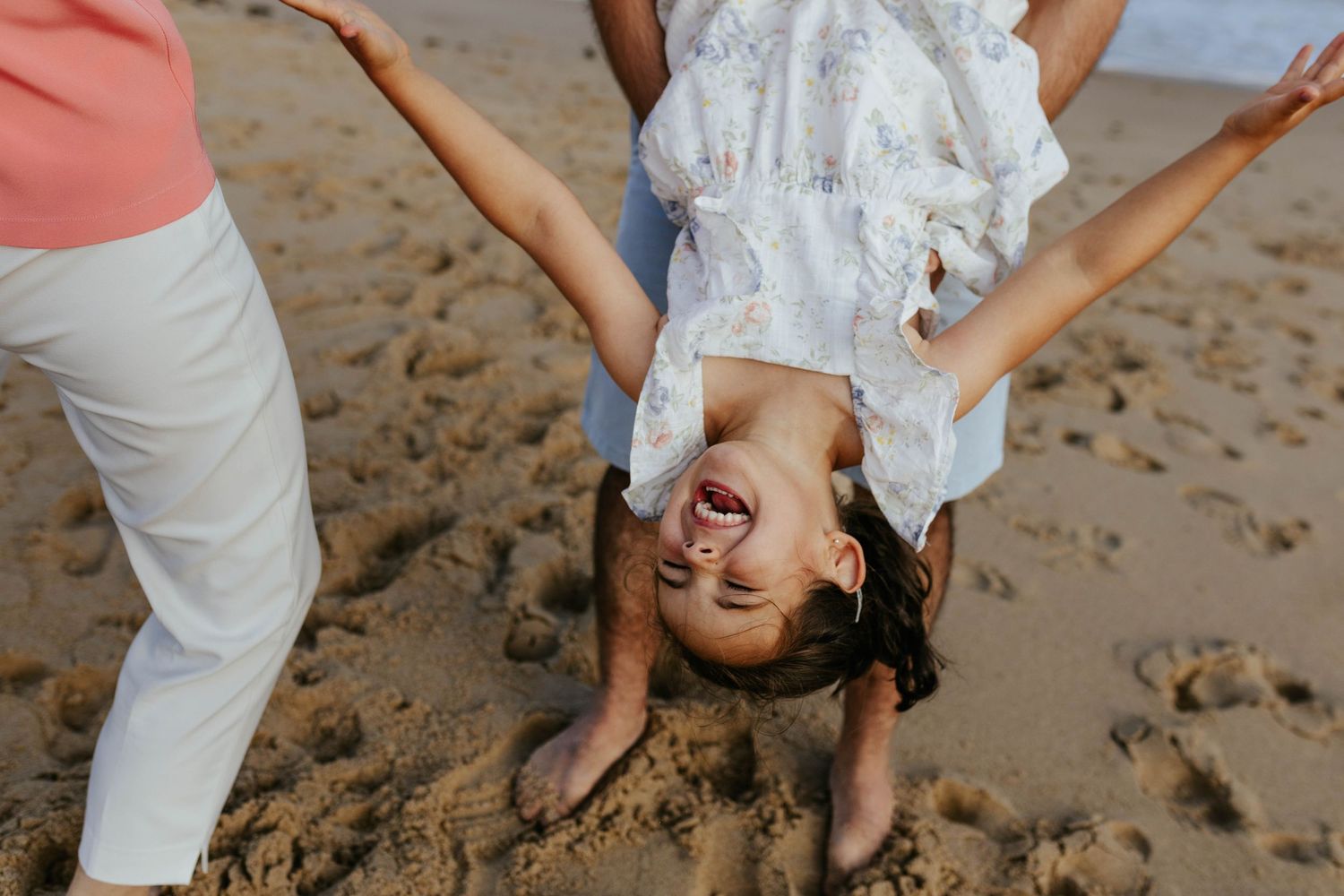 A playful moment captured on the beach as a child is held upside down in white clothing.