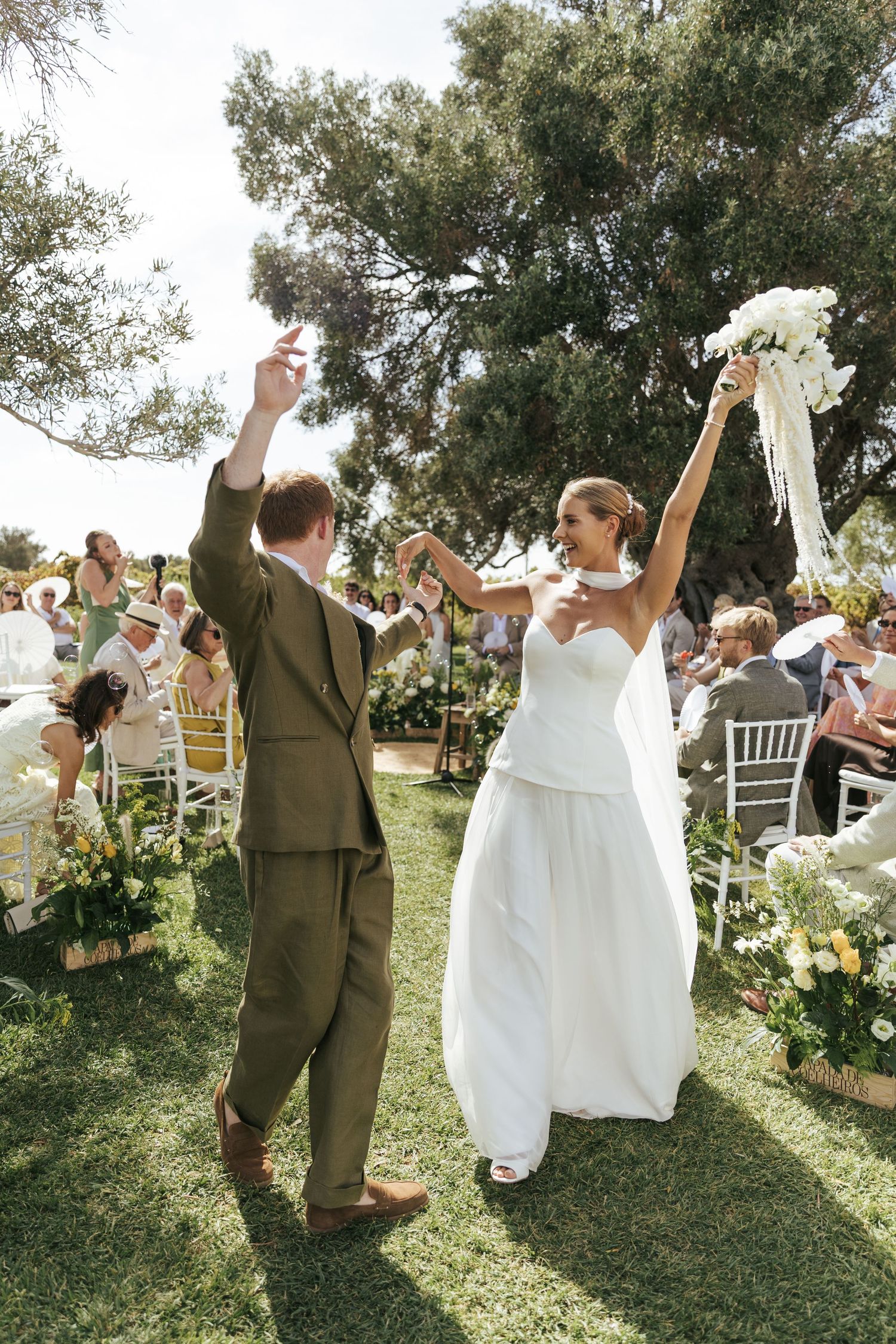Bride and groom celebrate joyfully walking back down the aisle at an outdoor wedding ceremony on a sunny day.