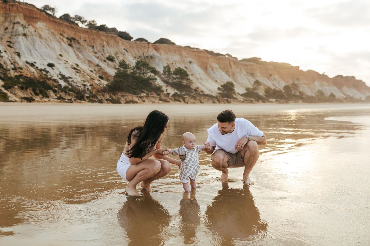 Family enjoys a sunset moment together on a beach with scenic cliffs in the background.