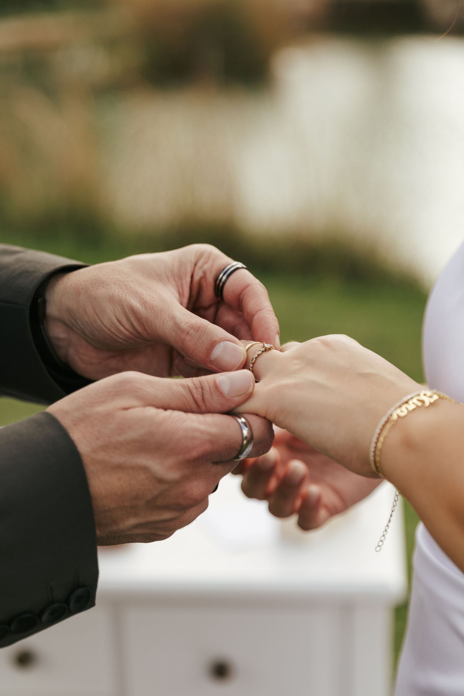 Close-up shot of hands exchanging wedding rings during an outdoor ceremony.
