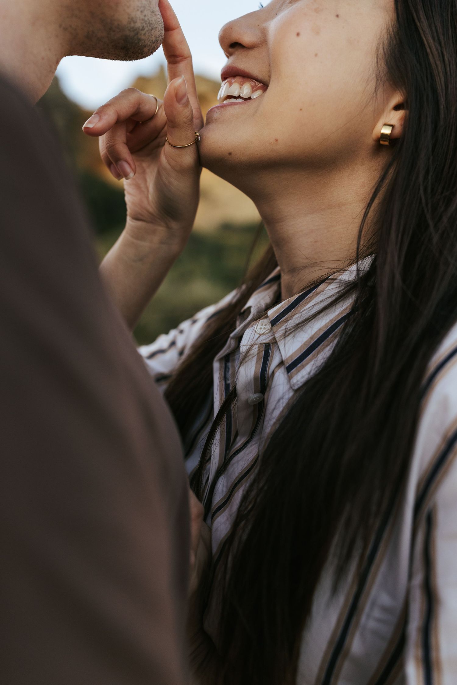 Close-up view of someone wearing a striped shirt laughing joyfully outdoors with long dark hair.