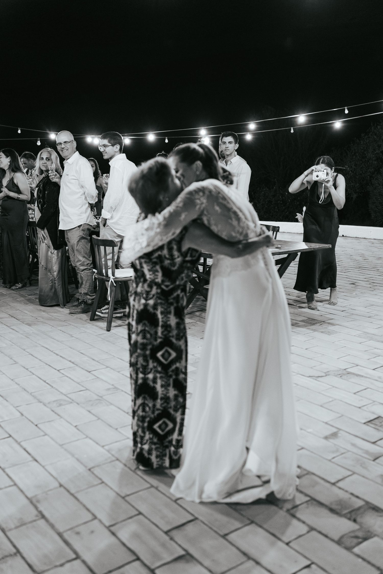 Wedding guests dance together on an outdoor patio under twinkling string lights at night.