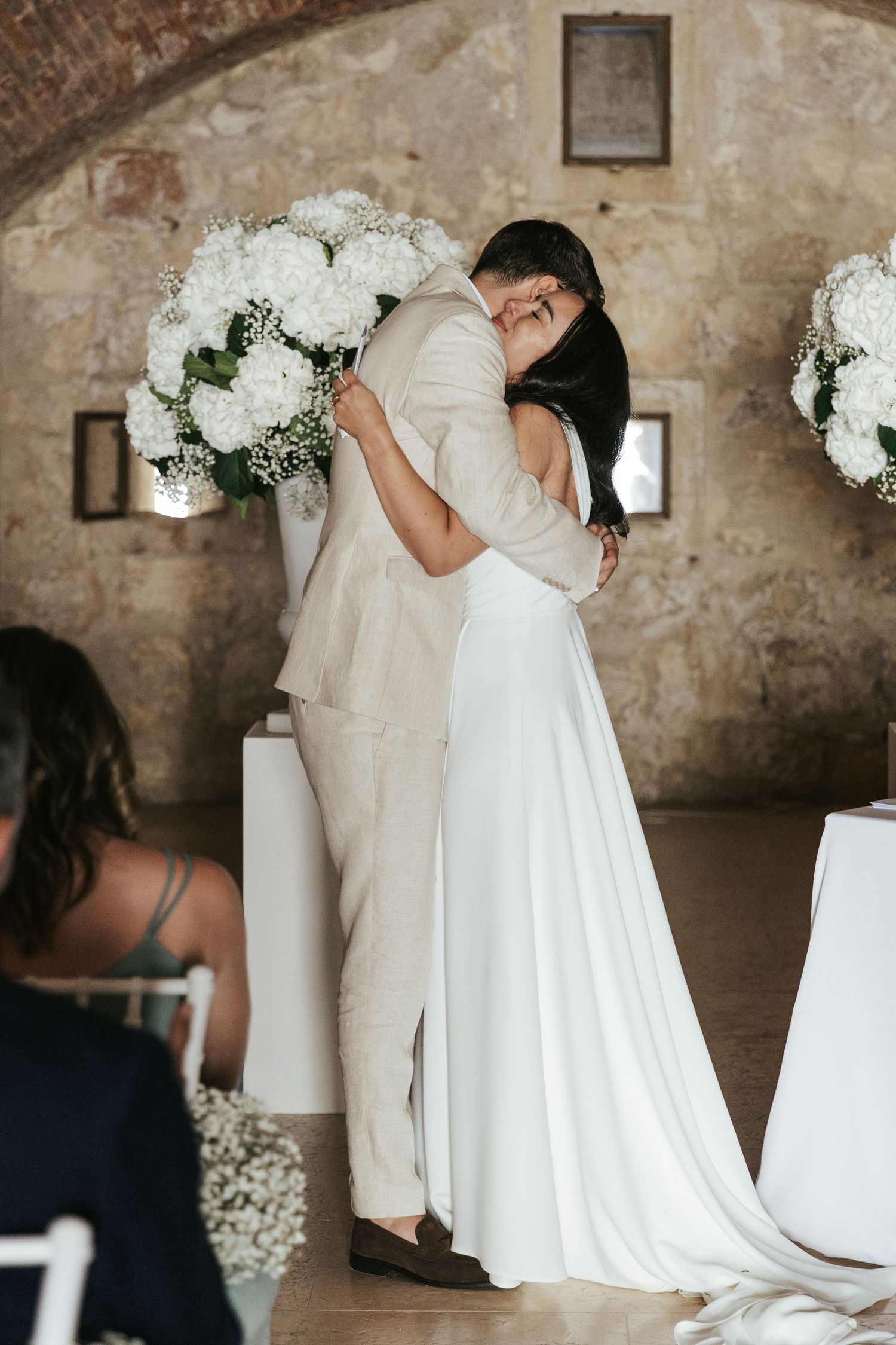 Wedding ceremony setup with white floral arrangements and chairs in rustic brick venue.