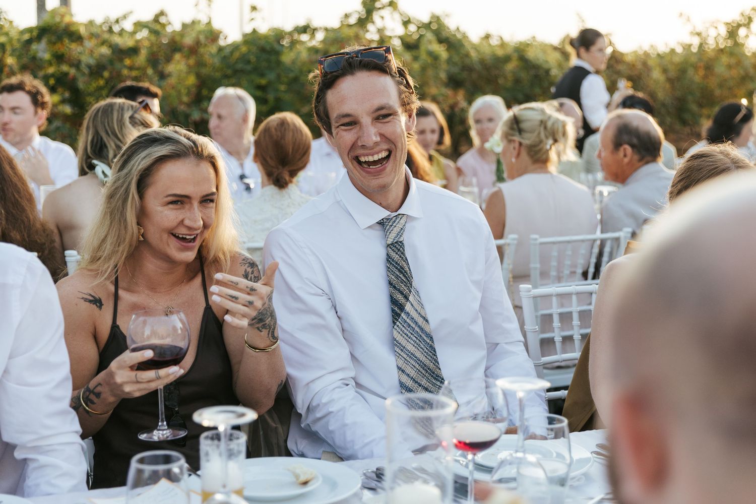 Couple laughing and enjoying wine at an outdoor wedding reception dinner party.