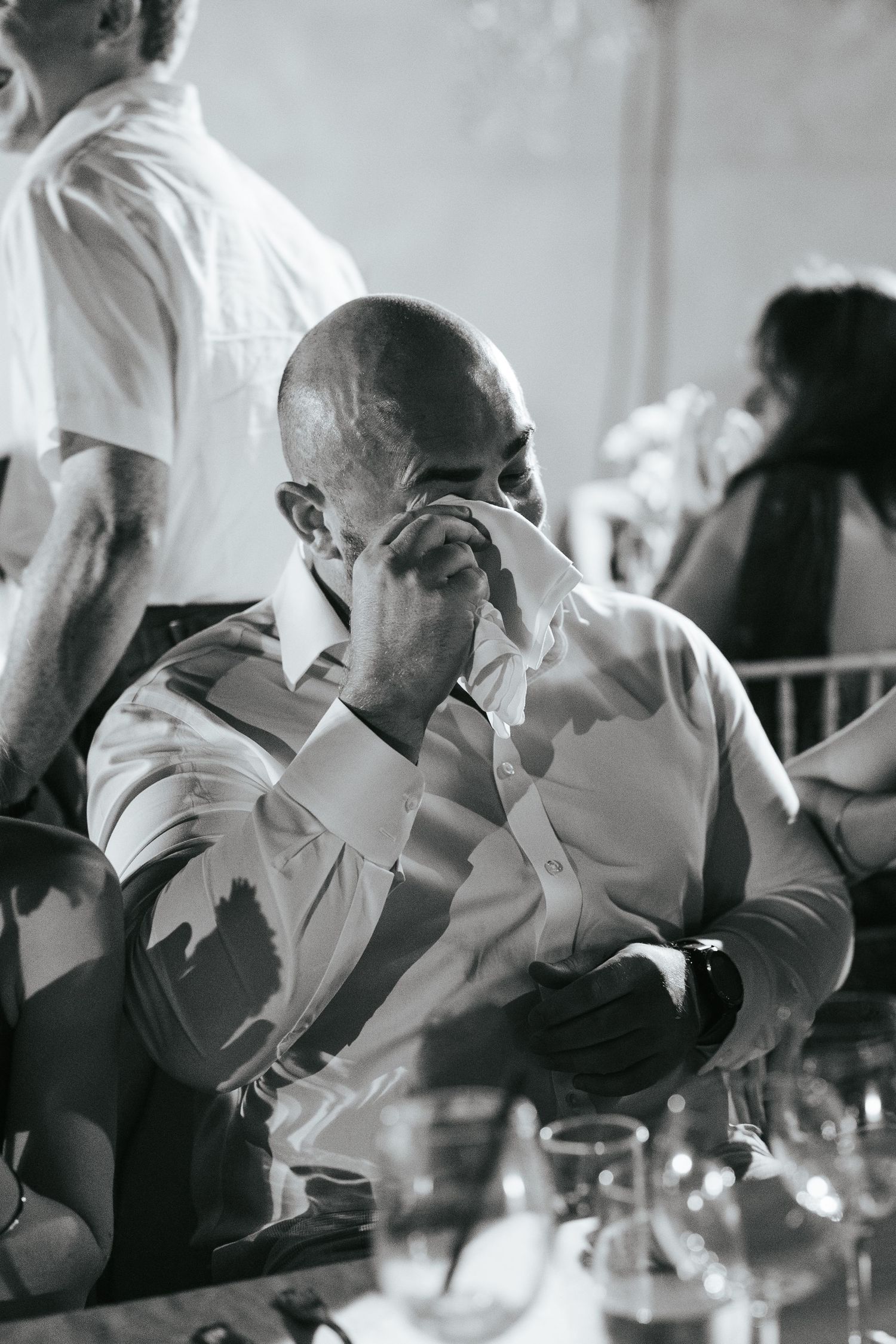 Emotional bald man wiping tears at a wedding reception, black and white photo.