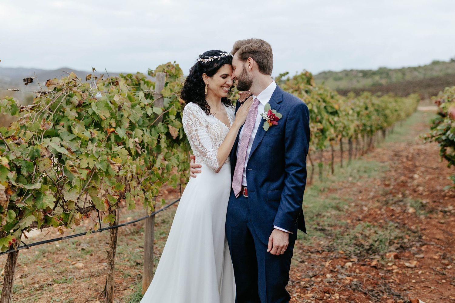 A romantic bride and groom share a tender moment among the rows of grapevines at a vineyard on their wedding day.