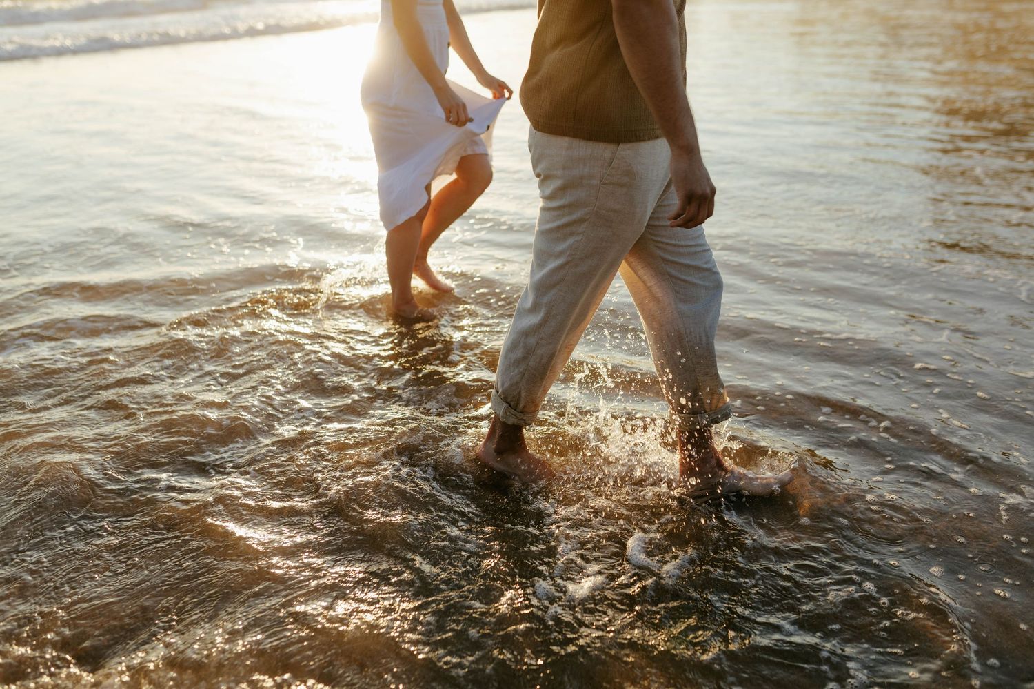 Feet splashing in shallow ocean waves during sunset with golden light reflecting on the water.