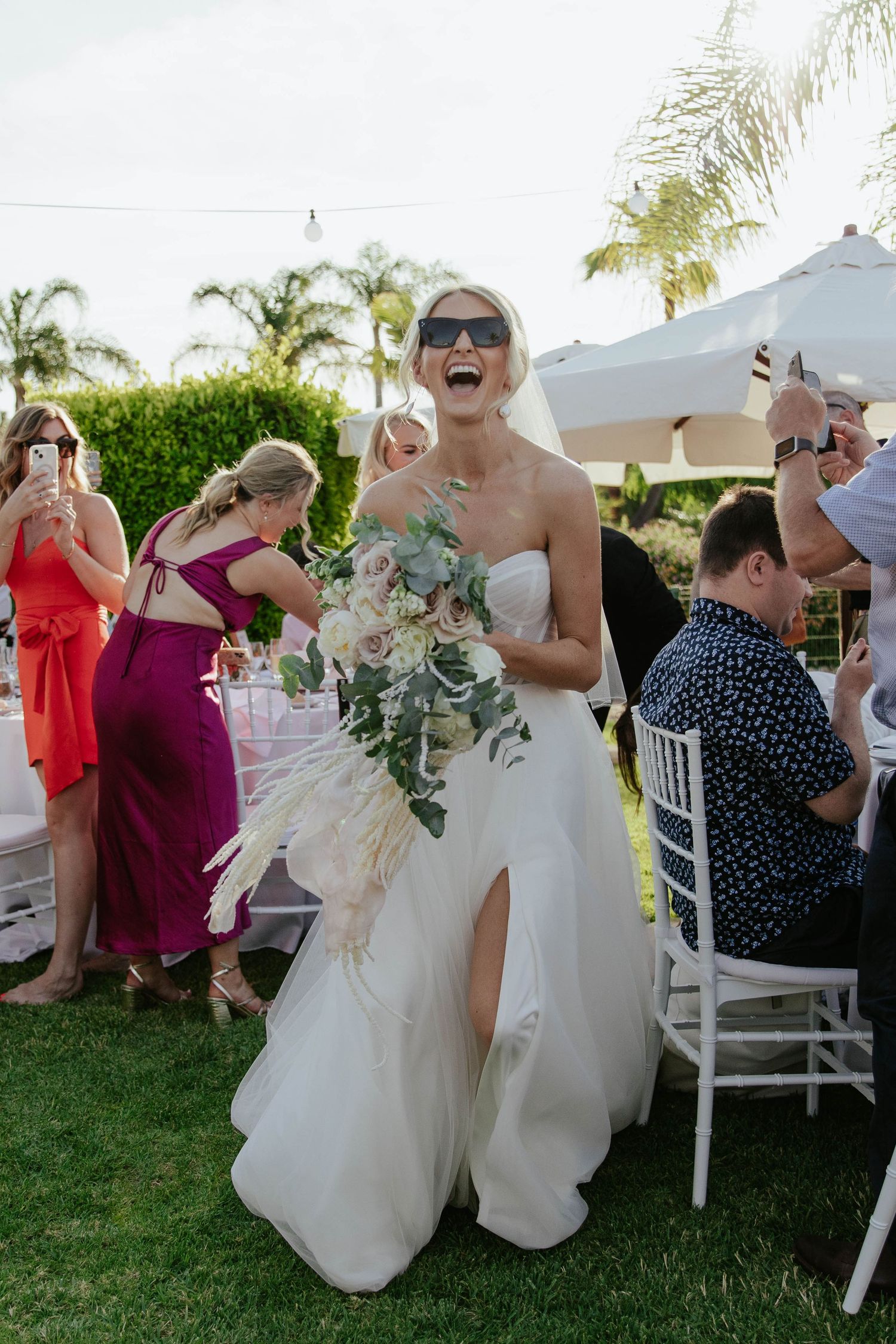 Joyful bride in strapless white gown laughing during outdoor garden reception.