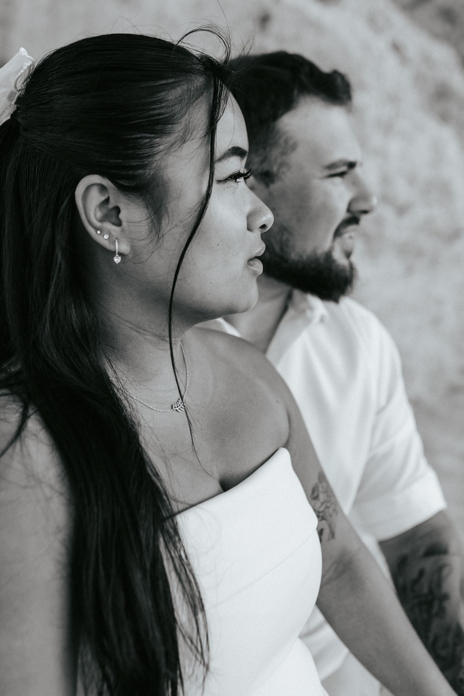 Black and white profile photo of couple in white clothing against light colored wall, showing side view.