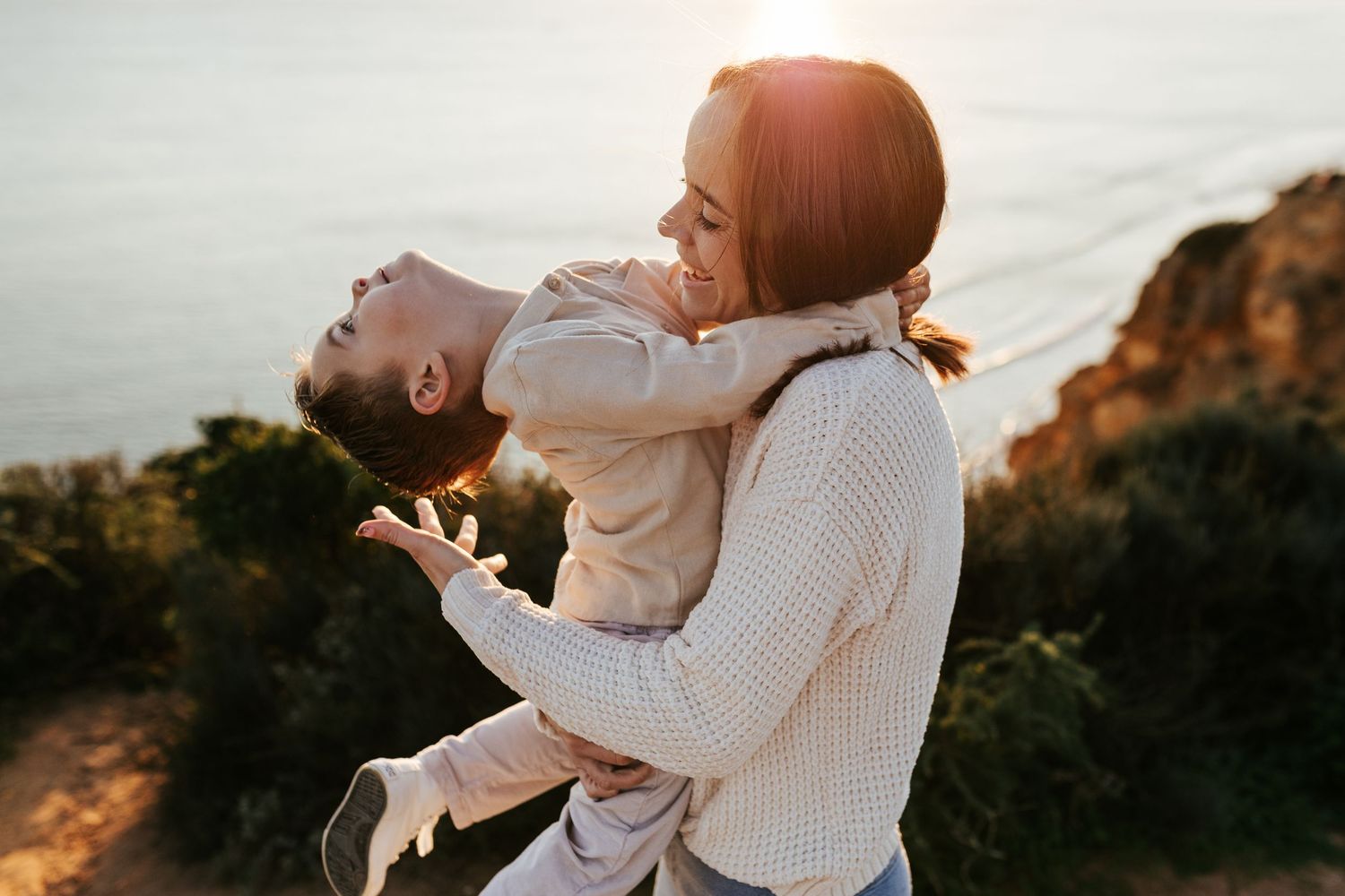 Two people share a joyful embrace while wearing white sweaters against a sunset mountain backdrop.