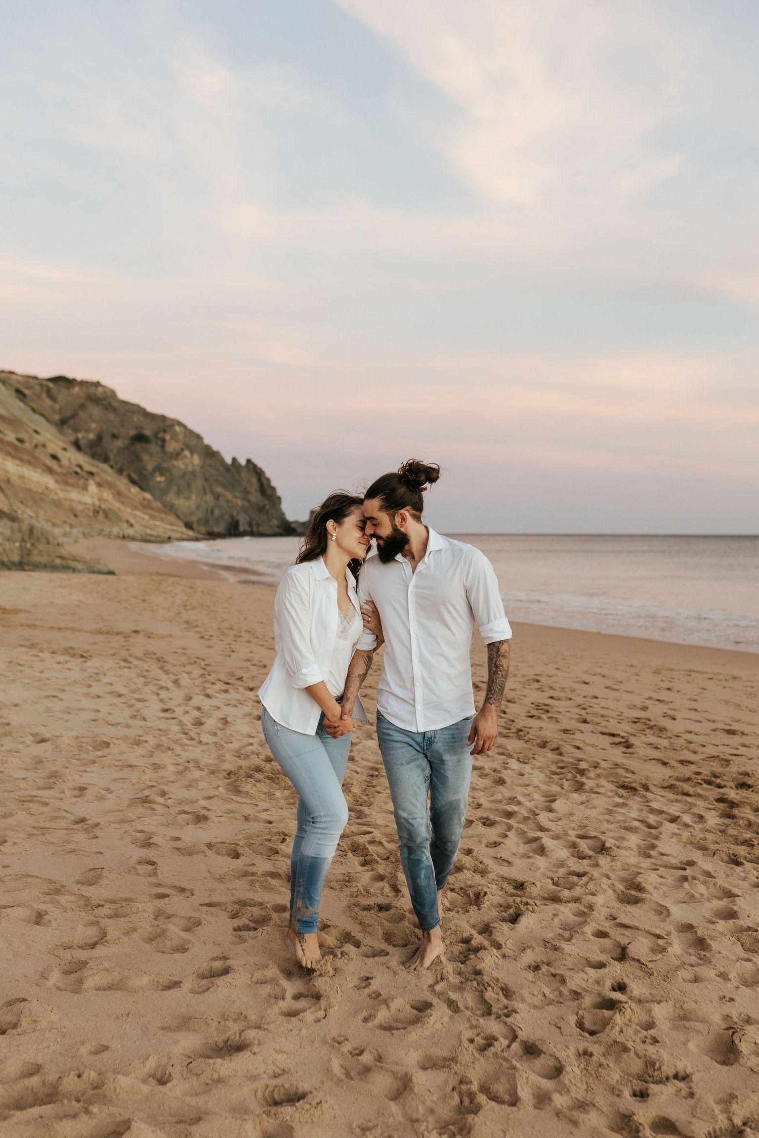 A couple walking barefoot together on a scenic beach with cliffs in the background. Praia da Luz, Lagos, Algarve, Portugal.