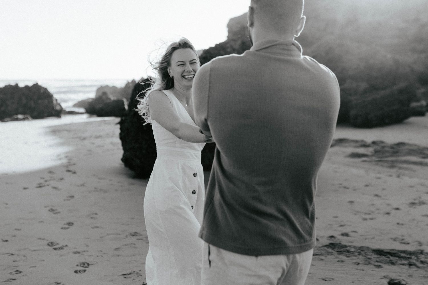Black and white candid photo showing couple dancing together on beach.