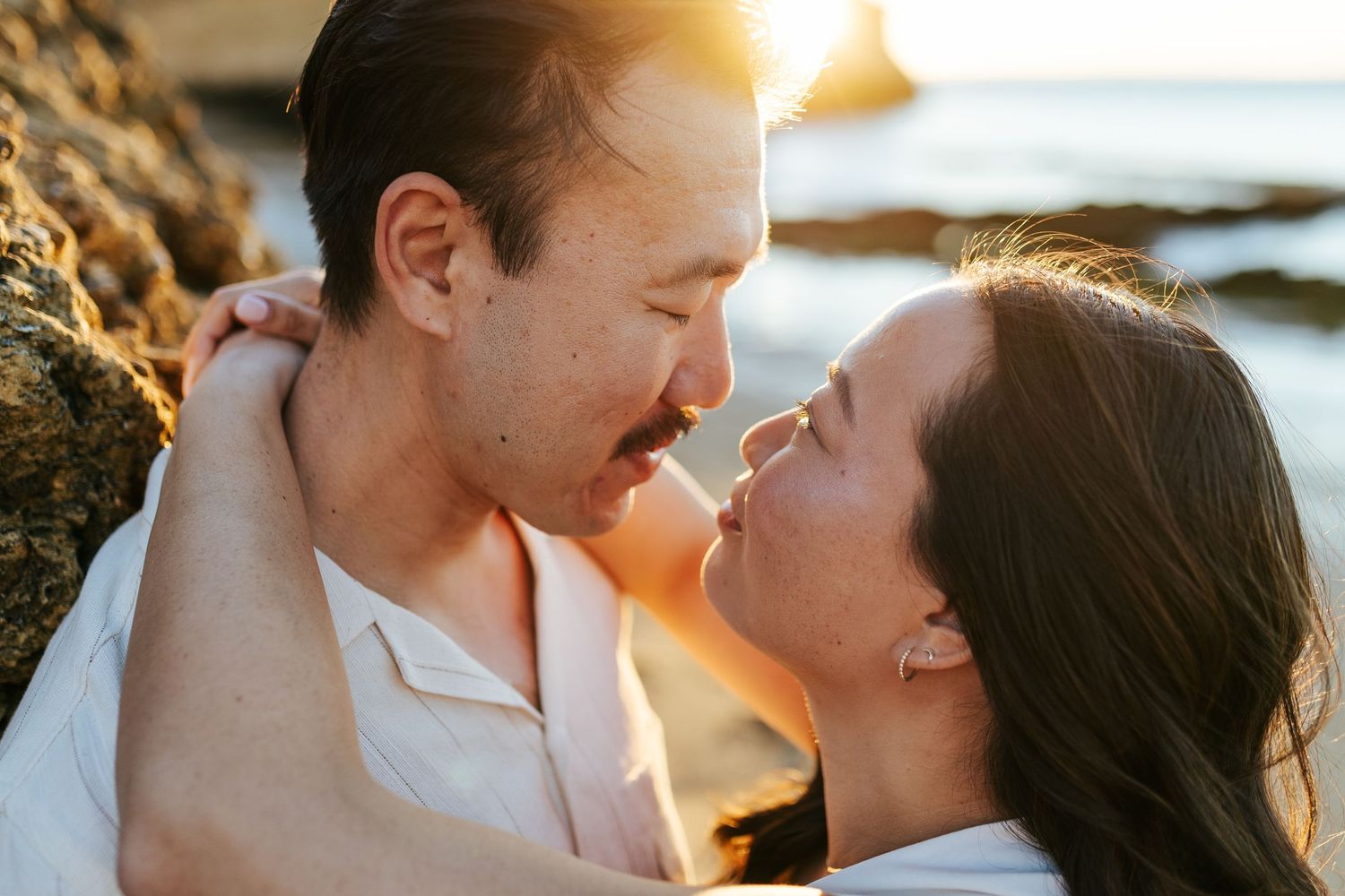 A romantic couple shares an intimate moment at sunrise against a coastal backdrop. Praia Dona Ana, Lagos, Algarve, Portugal.