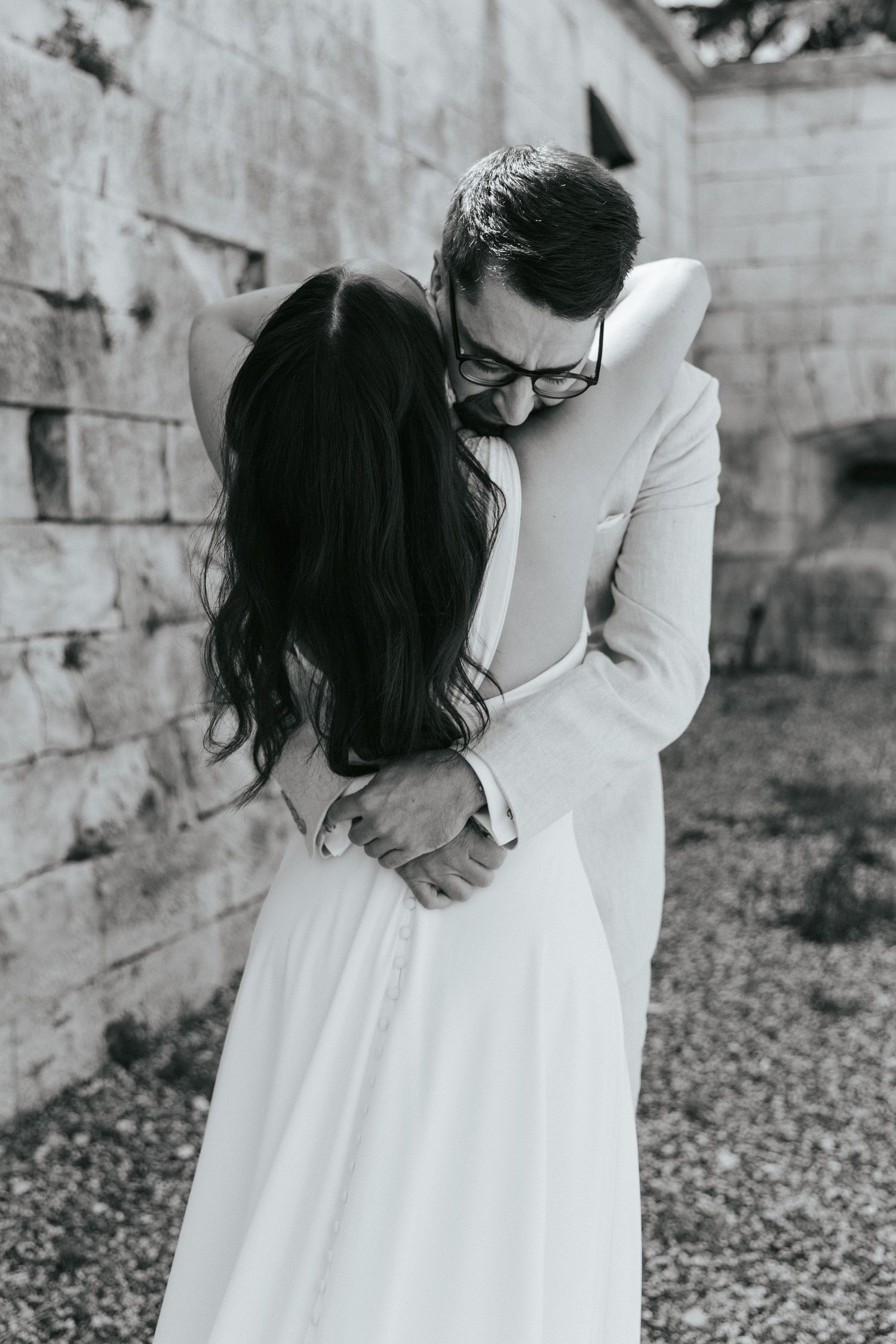 Black and white wedding photos capture tender moments between newlyweds against stone walls.