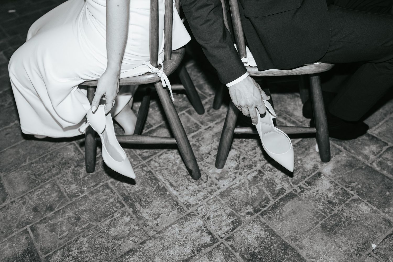 Black and white vintage photograph showing feet in high heeled shoes beneath tables and chairs on a wooden floor.