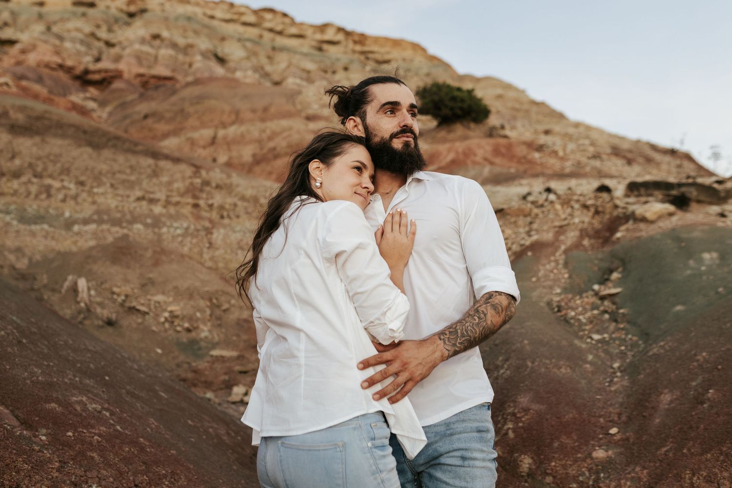 A couple embraces against a backdrop of dramatic coastal cliffs. Praia da Luz, Lagos, Algarve, Portugal.
