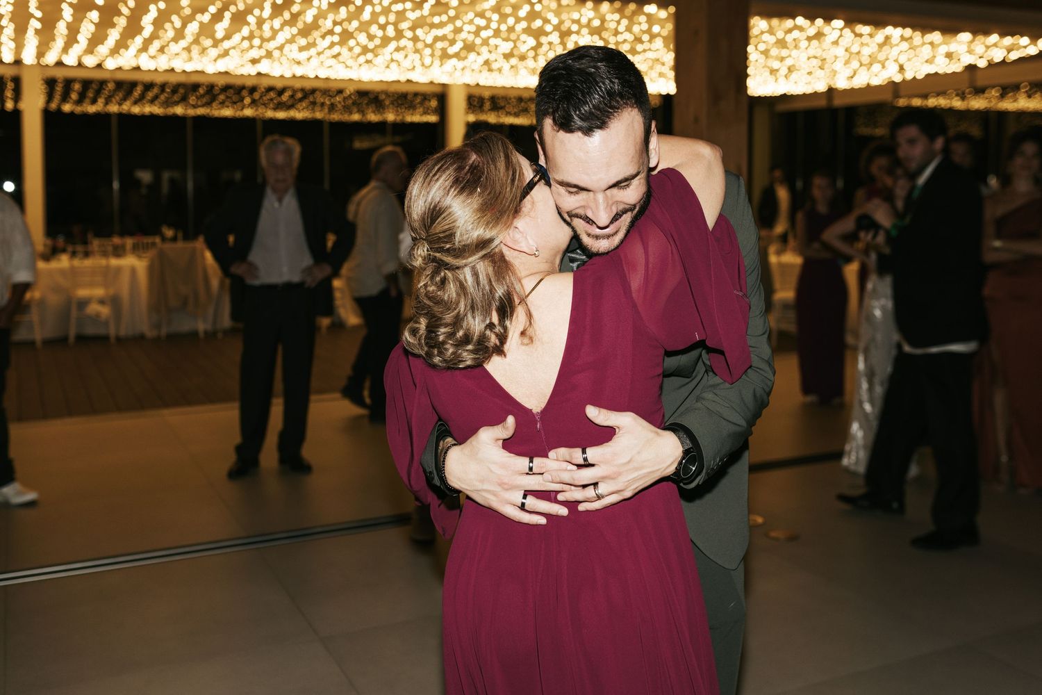 A couple shares an intimate dance moment beneath warm glowing string lights.