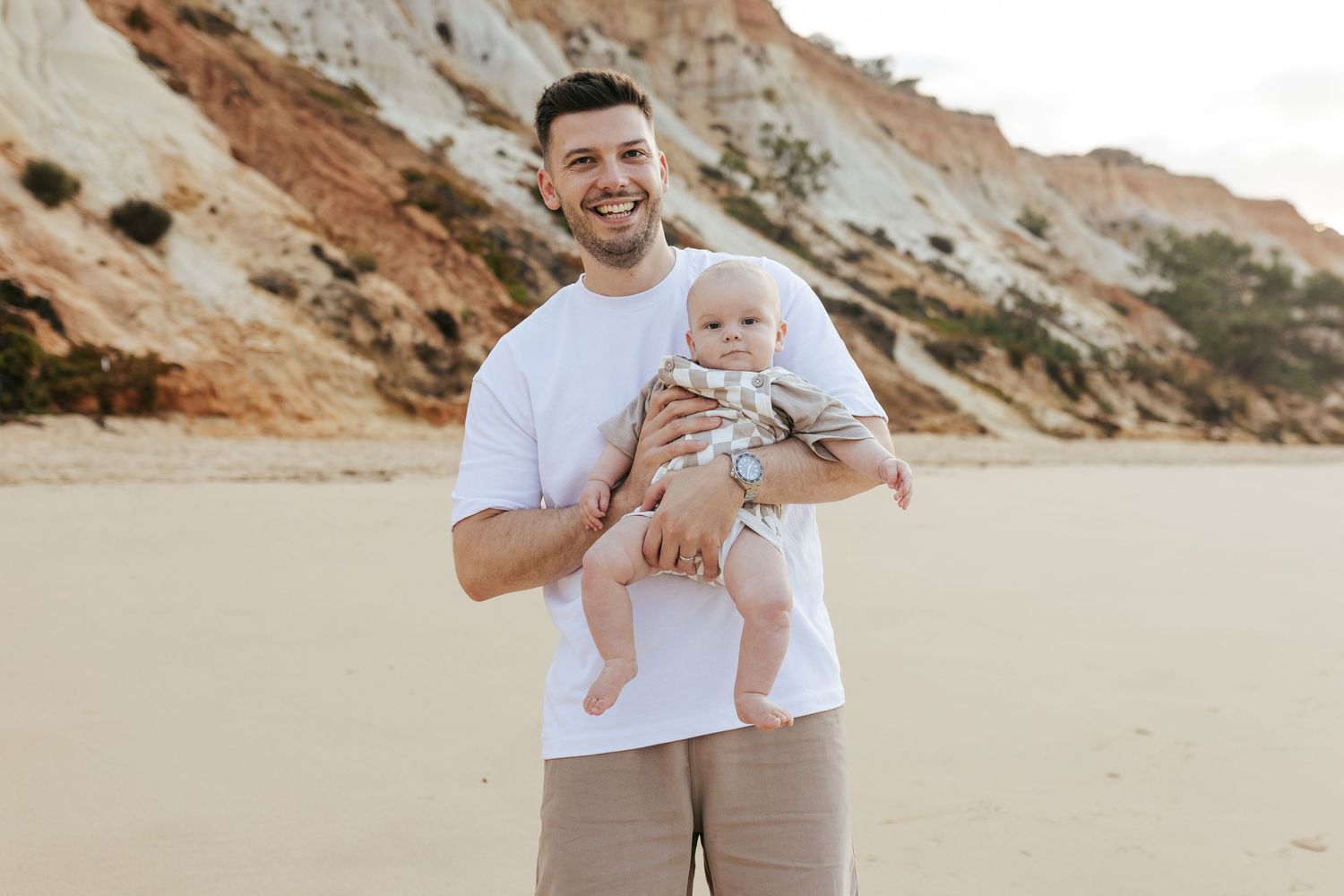 Two people standing on a beach with scenic orange cliffs in the background.