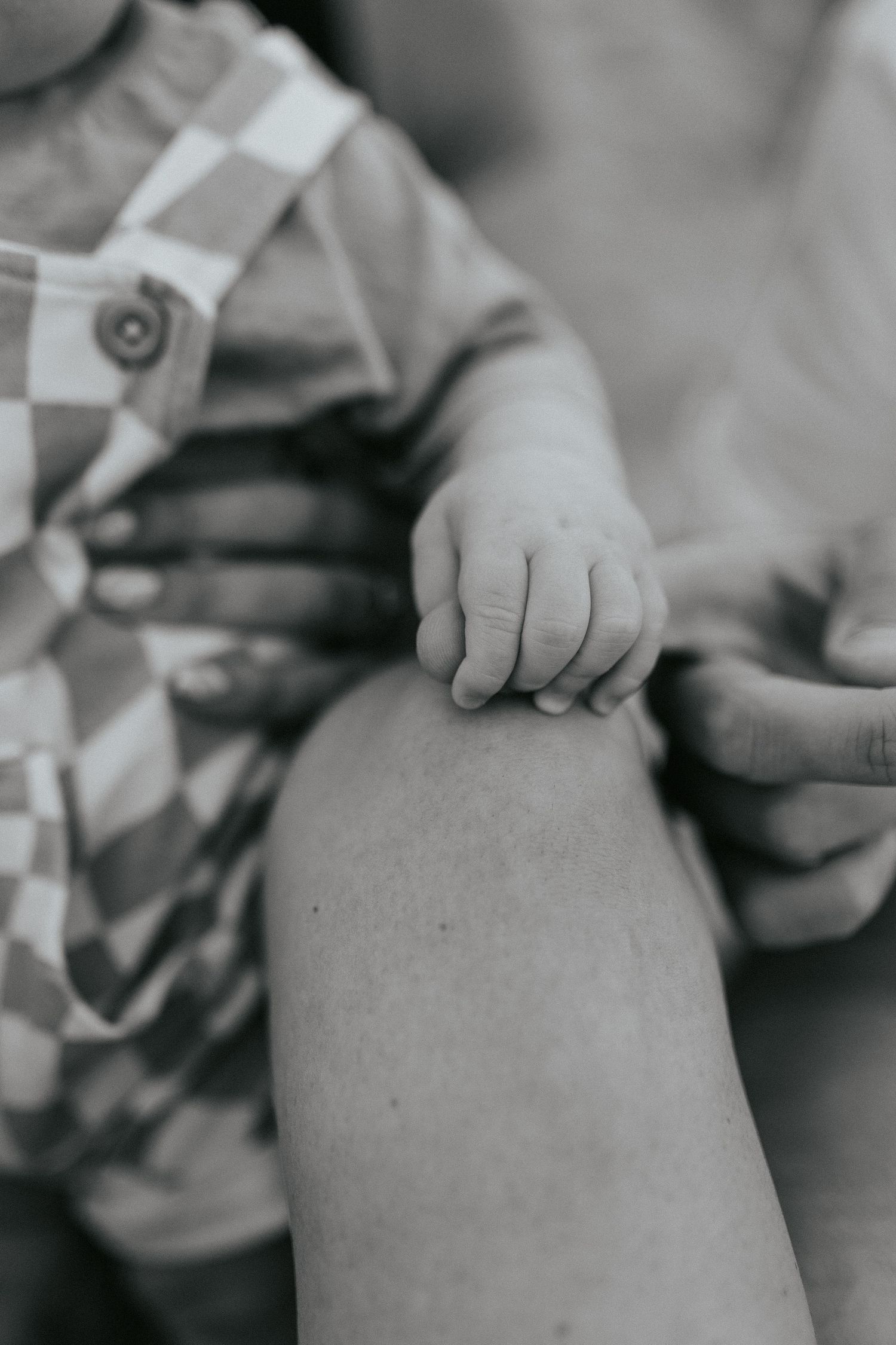 Black and white closeup of a small child's hand touching a person's knee in soft focus.