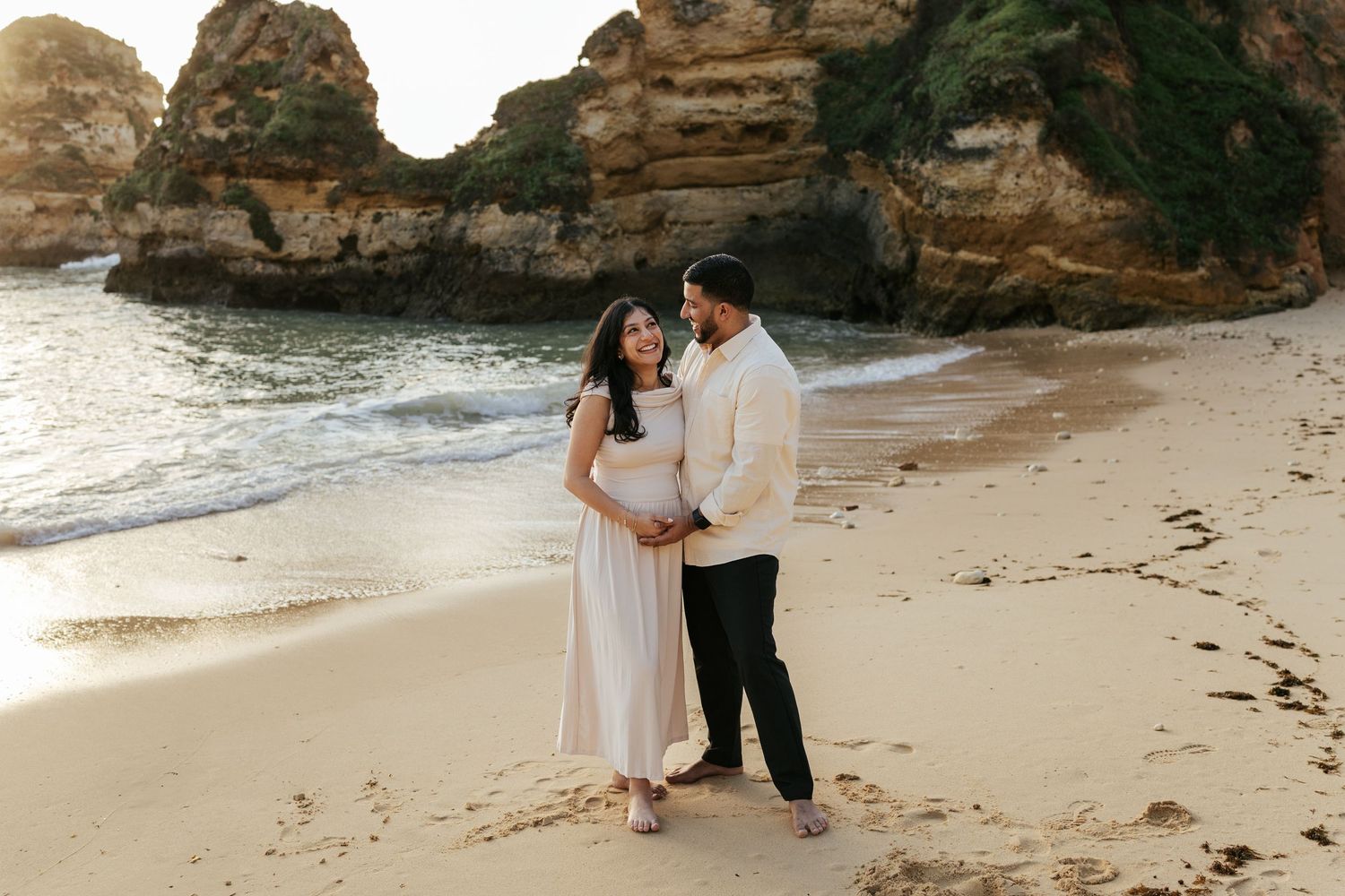 Couple shares tender moment on beach with scenic rocky coastline in background. Praia do Camilo, Lagos, Algarve, Portugal.