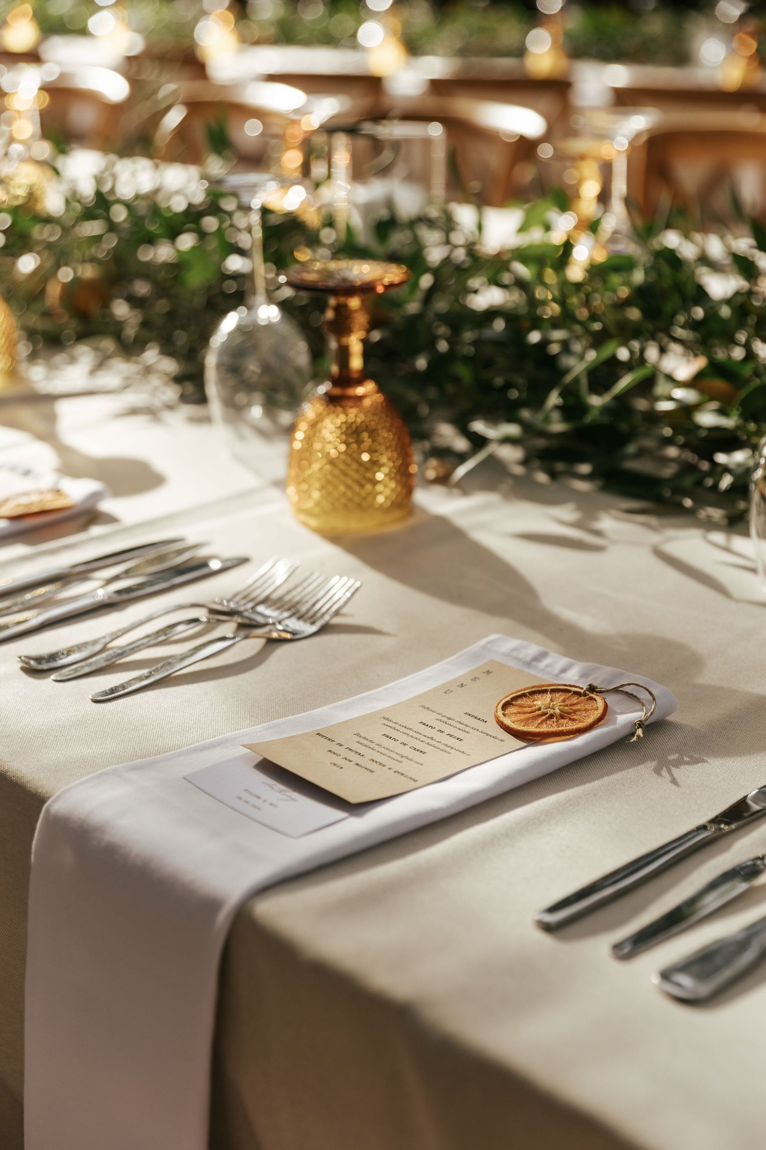 Elegant wedding table setting with white linens, silverware, and greenery garland decorations in warm lighting.