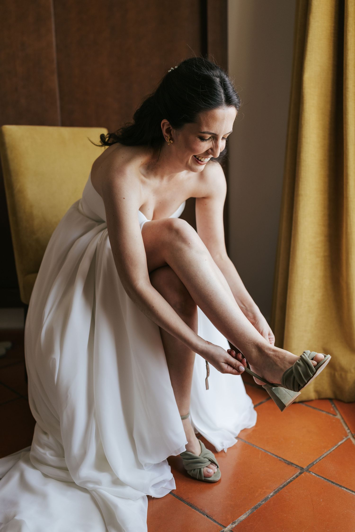 Person in white dress sits on terracotta floor while putting on shoes in sequence of four similar poses.