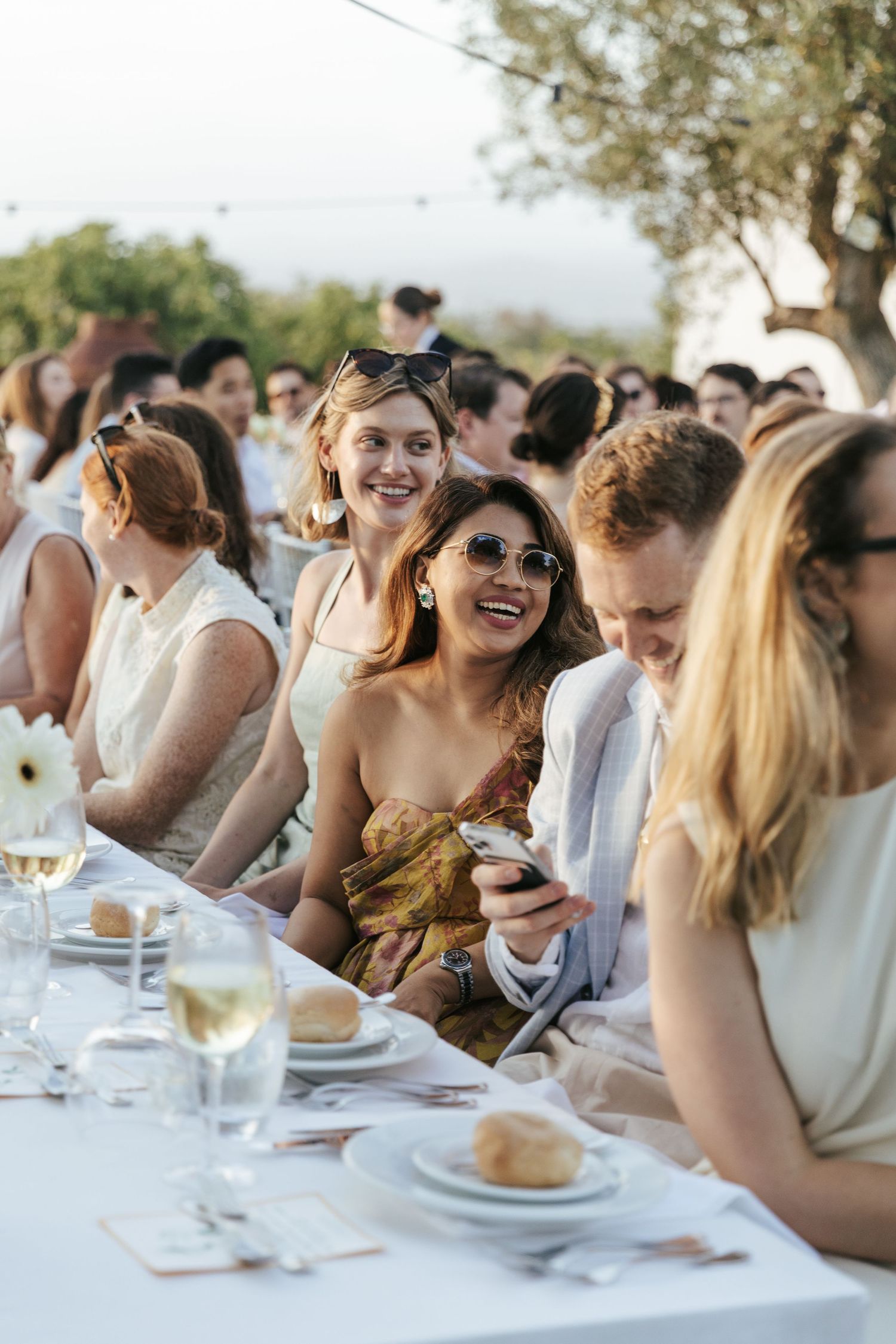 Guests laughing and enjoying wine at an elegant outdoor wedding reception dinner.