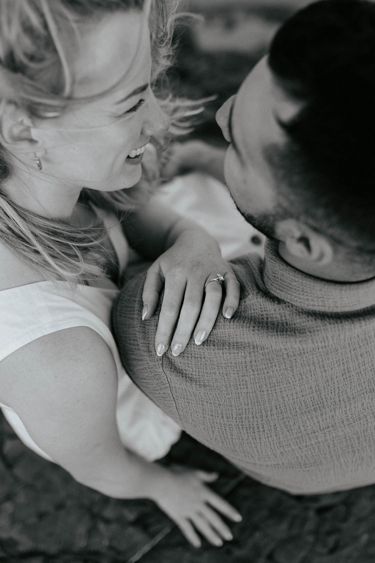 A tender black and white portrait showing an intimate moment as a couple embraces, with a close-up on her hand resting on his sweater.