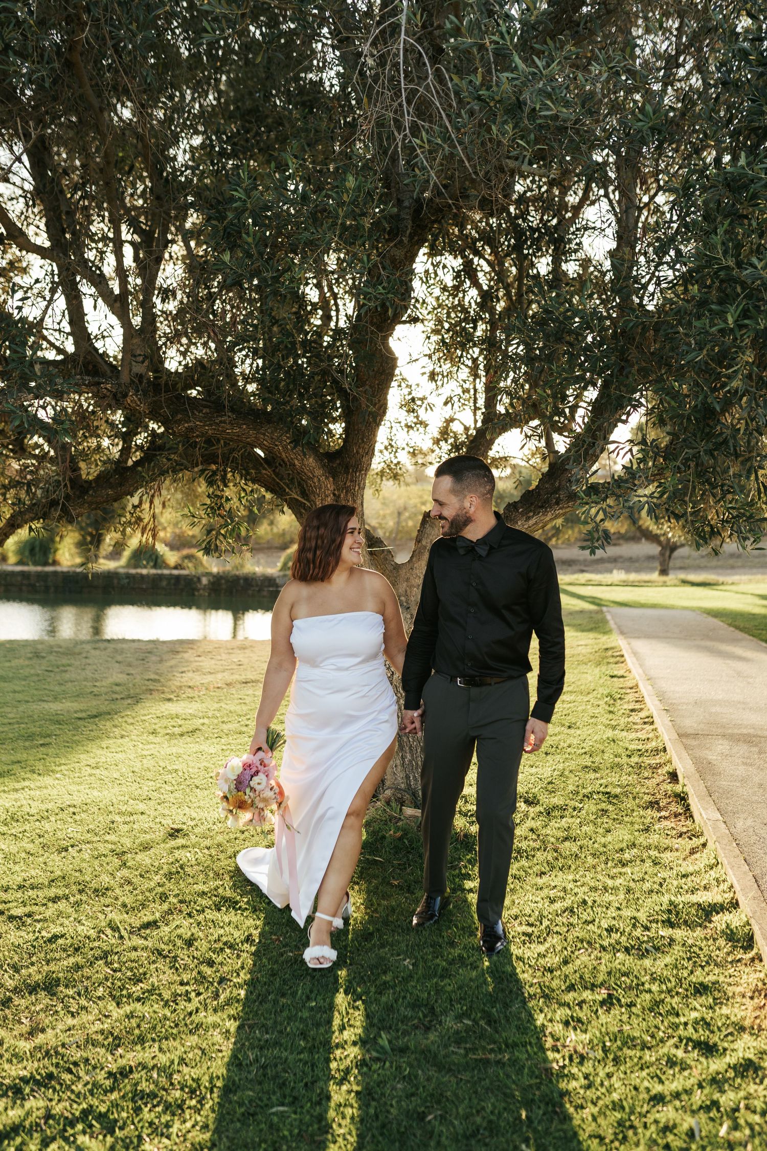 Couple takes romantic sunset stroll under oak trees on their wedding day.