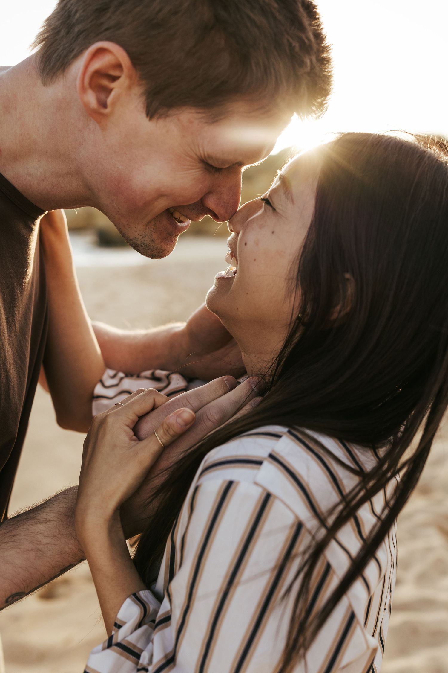 A couple shares an intimate moment laughing together in golden sunlight, with her wearing a striped shirt.
