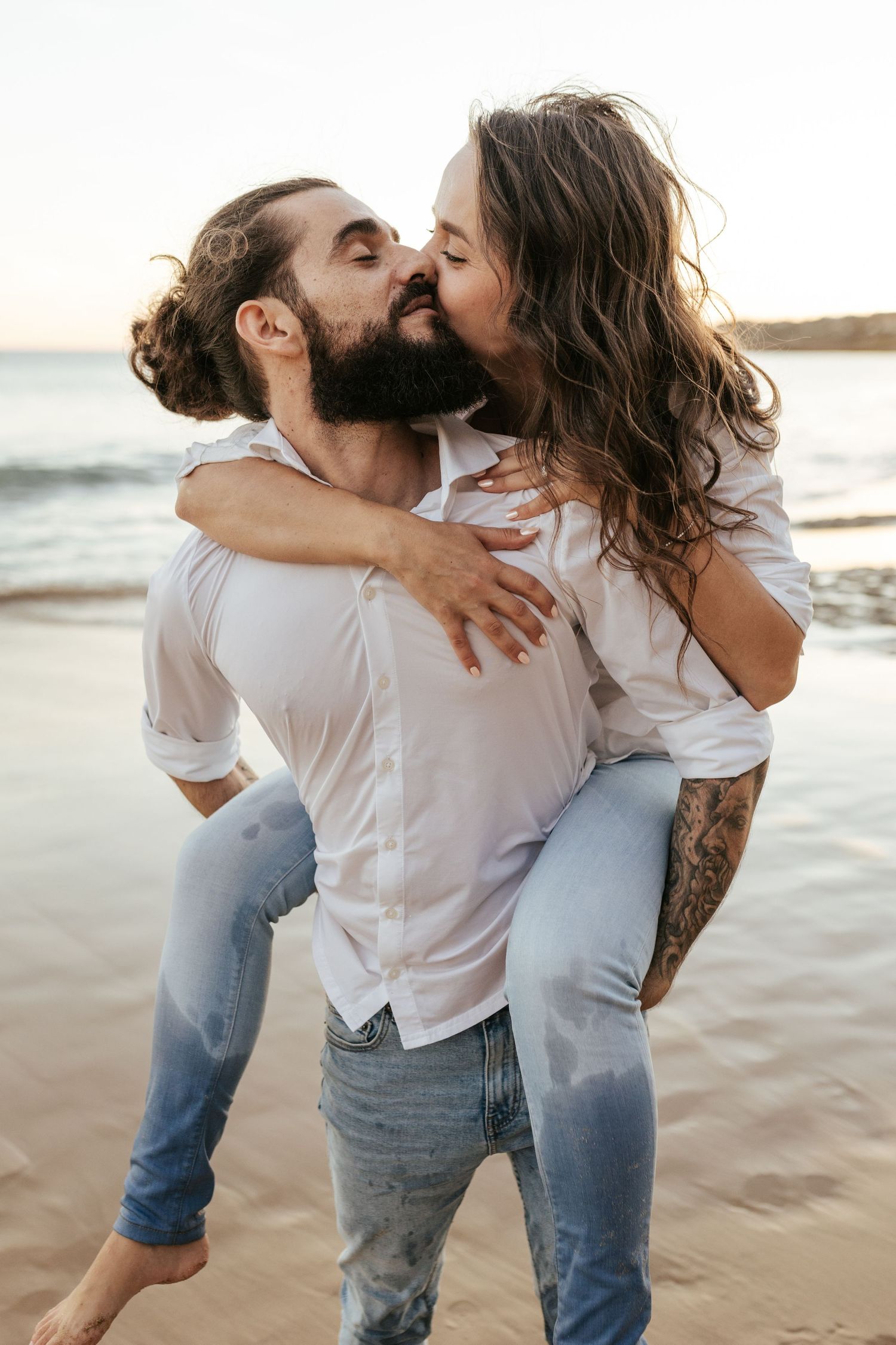 A couple shares a playful piggyback ride moment on the beach at sunset. Praia da Luz, Lagos, Algarve, Portugal.
