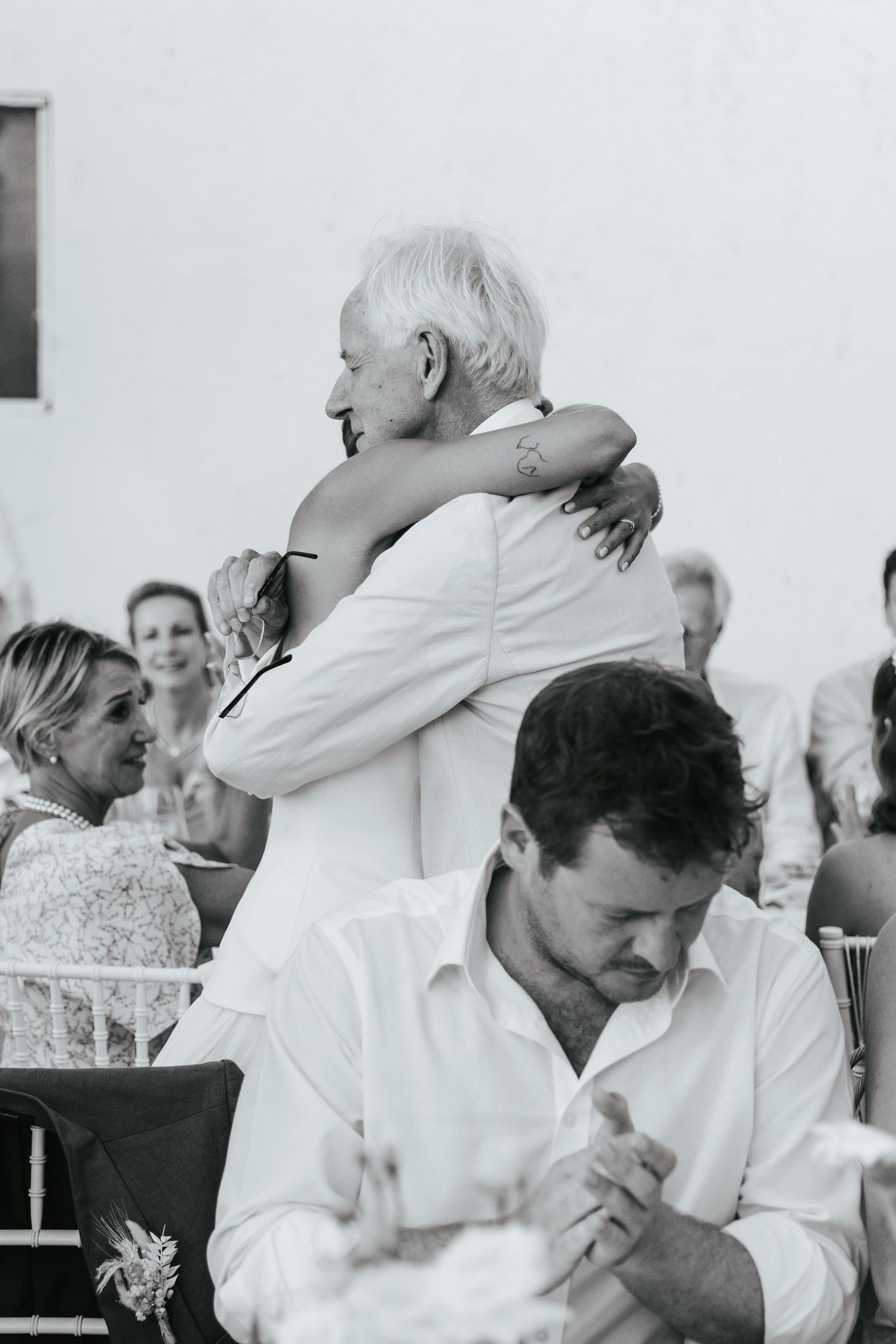 Black and white photo of an emotional wedding hug between bride and elderly guest at outdoor ceremony.