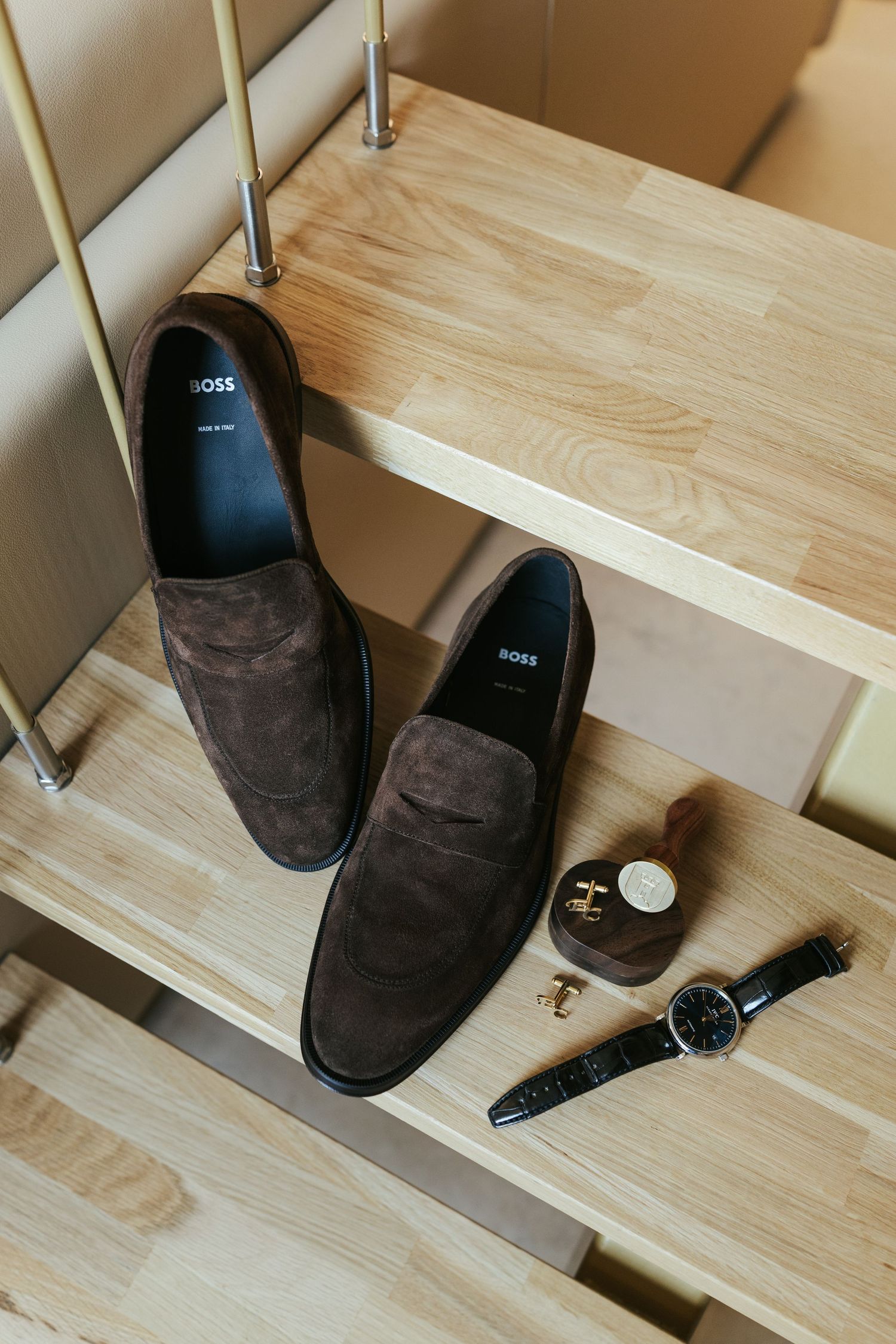 Brown suede boots and a watch arranged on a wooden shelf.