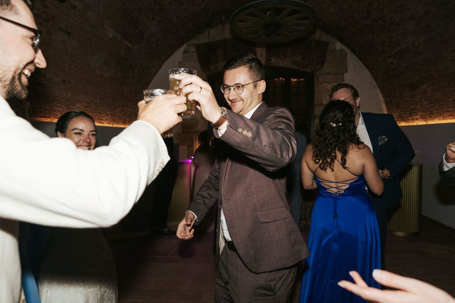 Wedding guests dancing energetically in a dimly lit reception venue.
