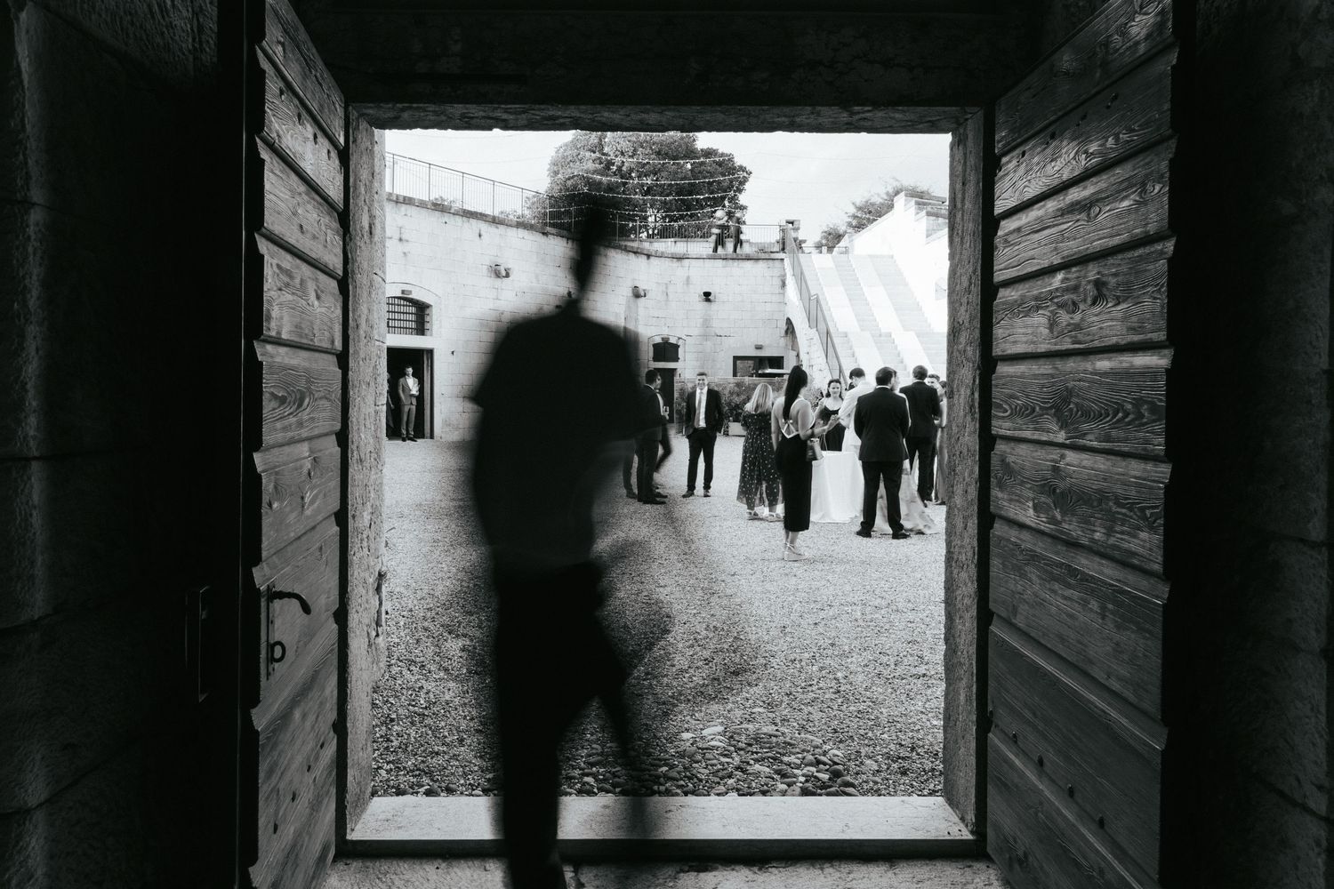 Artistic black and white shot through doorway frames wedding guests in the distance.