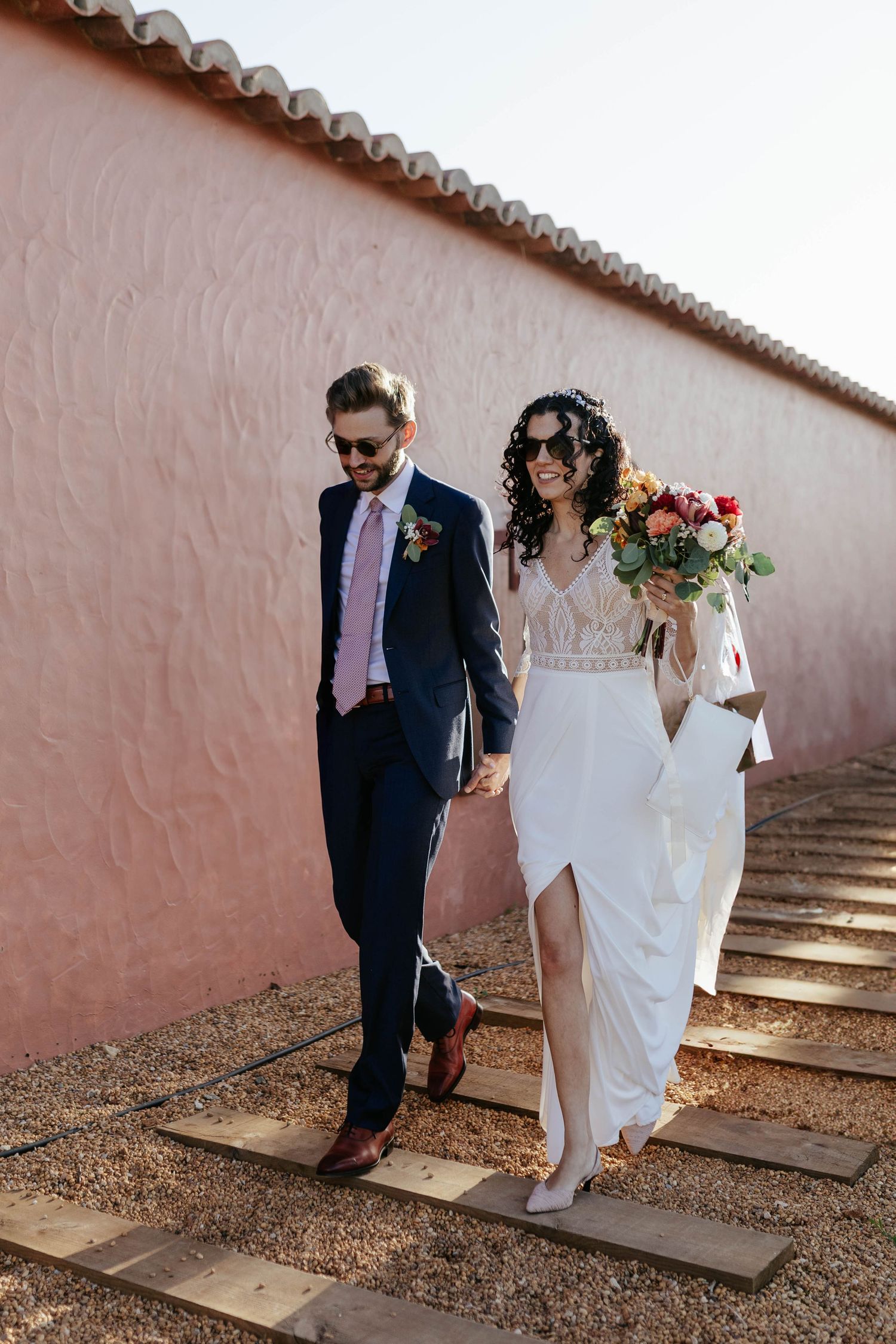 A couple walking together on stone steps during an outdoor wedding ceremony against a pink stucco wall.
