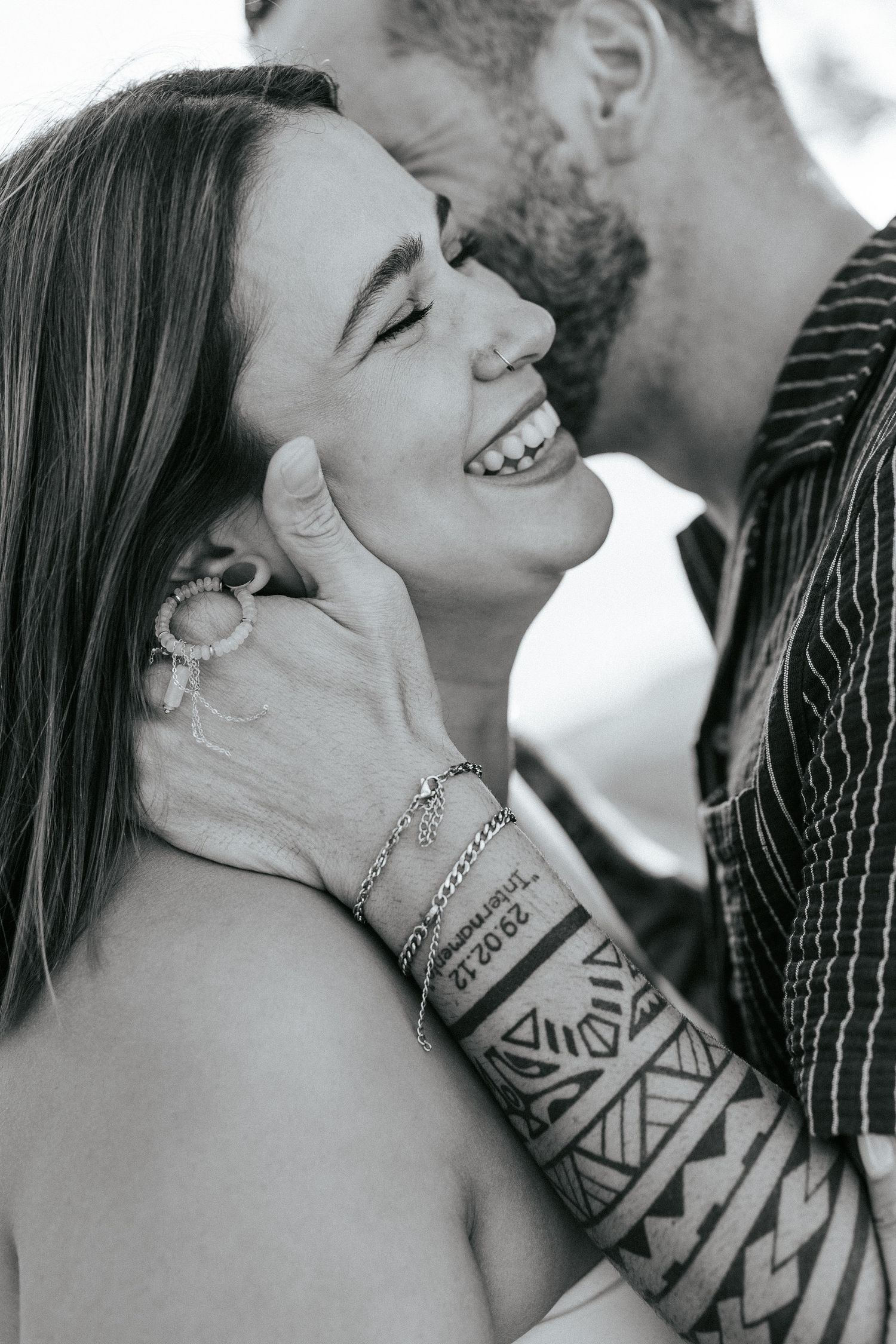 Black and white romantic close up photo showing a joyful smile and intricate geometric tribal tattoo sleeve.