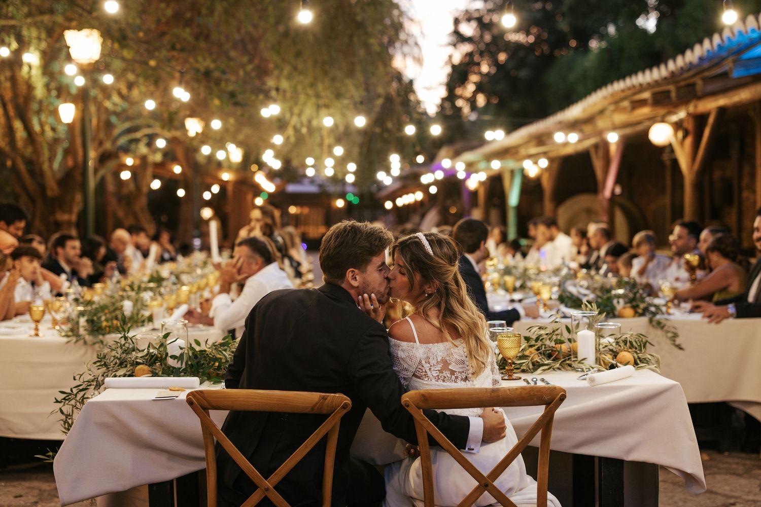 Elegant outdoor wedding reception at night with string lights illuminating tables set with white linens and floral centerpieces.