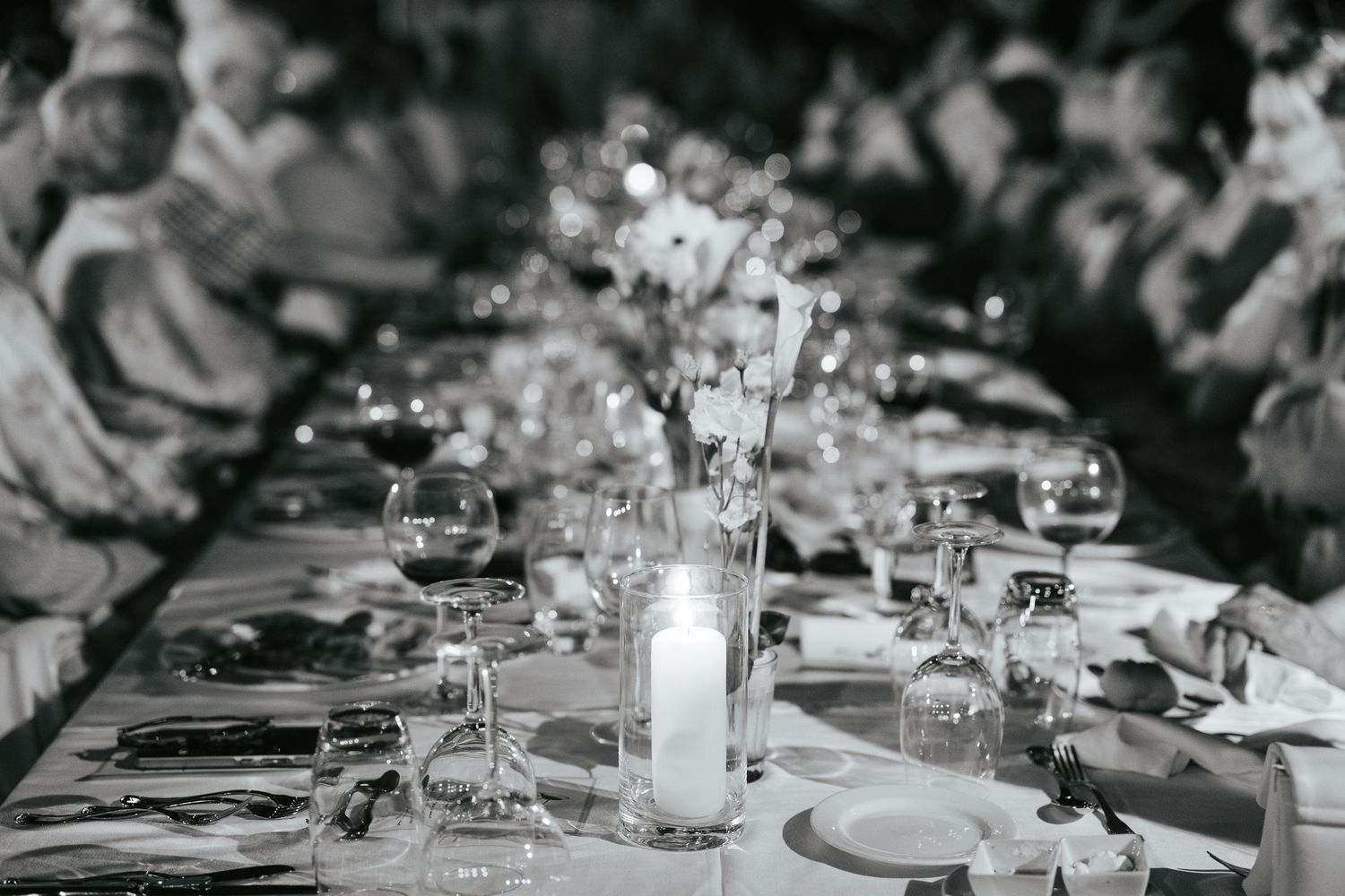 Elegant black and white wedding reception table with candles, crystal glasses, and floral centerpieces in soft bokeh.