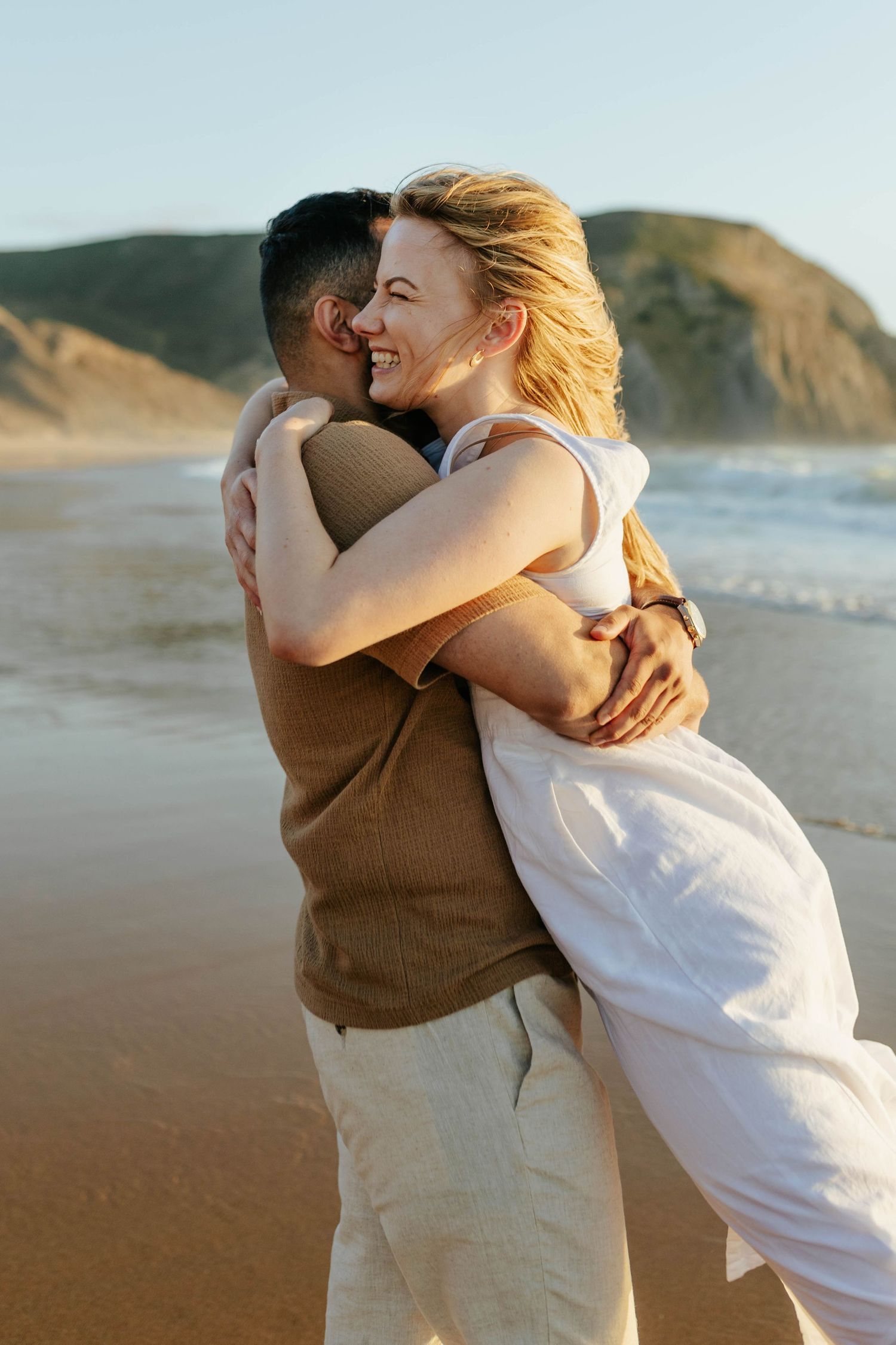 A tender embrace captured on a scenic beach with coastal cliffs in the golden hour light.